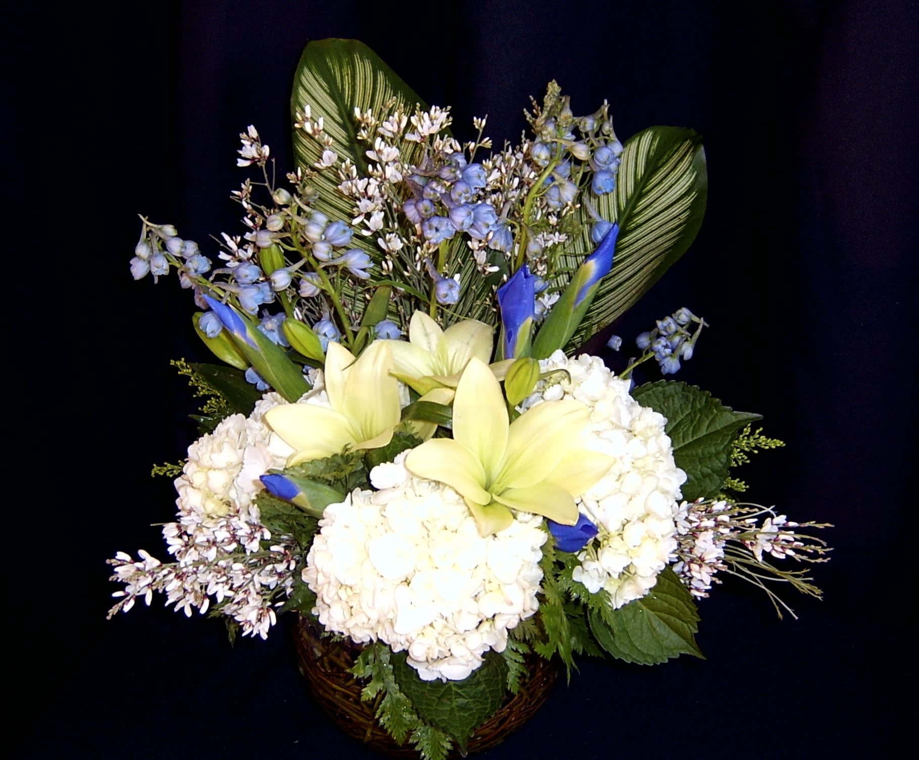 White hydrangeas and pale yellow lilies in a basket with blue accents