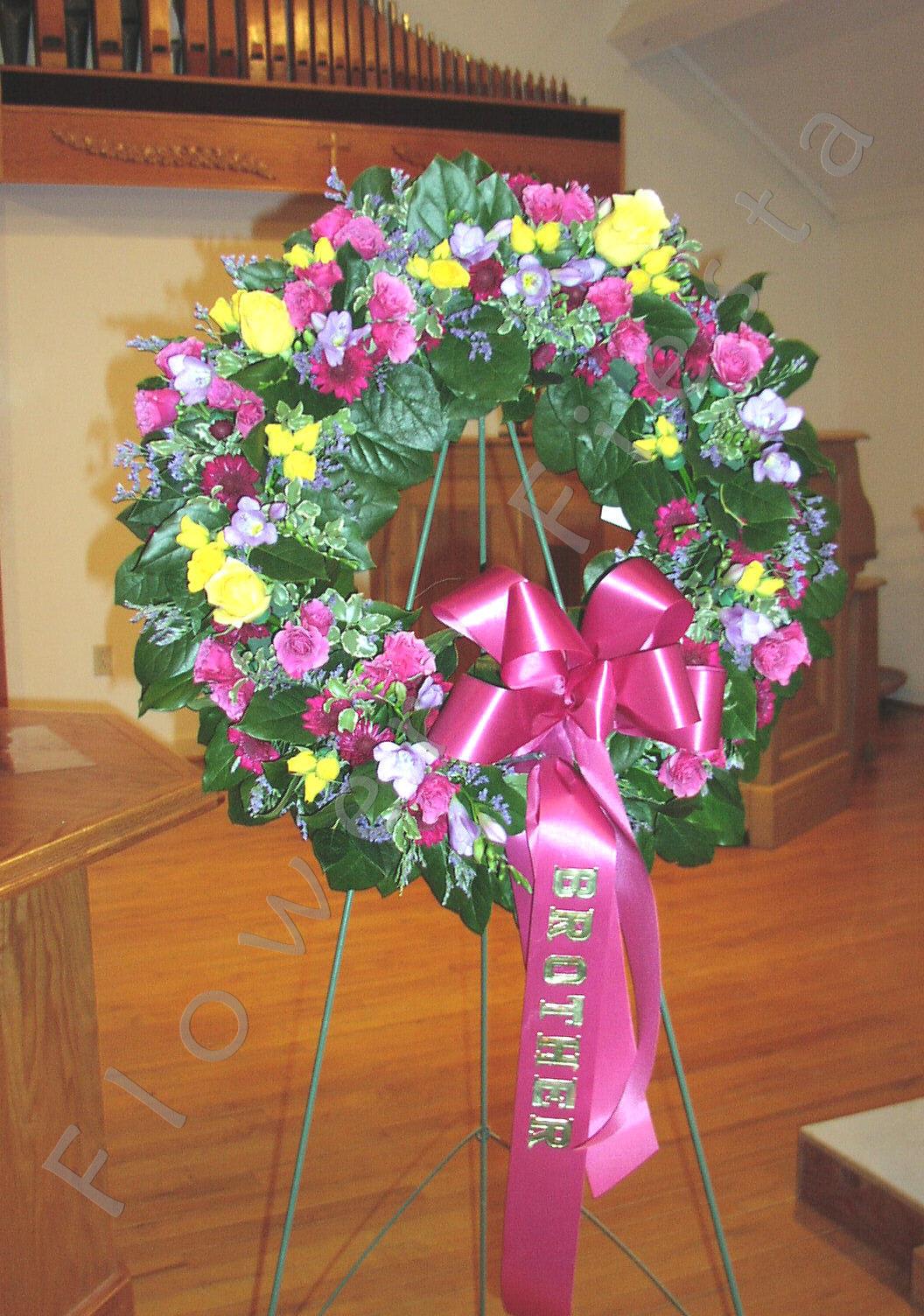 Sympathy Wreath Designer's Choice at a Discount, read description please - This wreath style is more affordable than our other wreaths and is a great choice for services that spring up when you don't have much notice to plan. We can make these quicker than a custom order wreath. WE WILL CHOOSE THE FLOWERS AND COLORS FOR YOU, depending what we have in stock or what we have an abundance of that needs to be used up quickly. The wreath will look nice on the day of delivery with flowers in full bloom but may not last a day longer for additional use later. There will be lots of foliage which also helps keep the cost down while looking fresh and serene.  Choose one word for the ribbon banner if you like. Include that word in The Notes or Special Reqests Section please. 