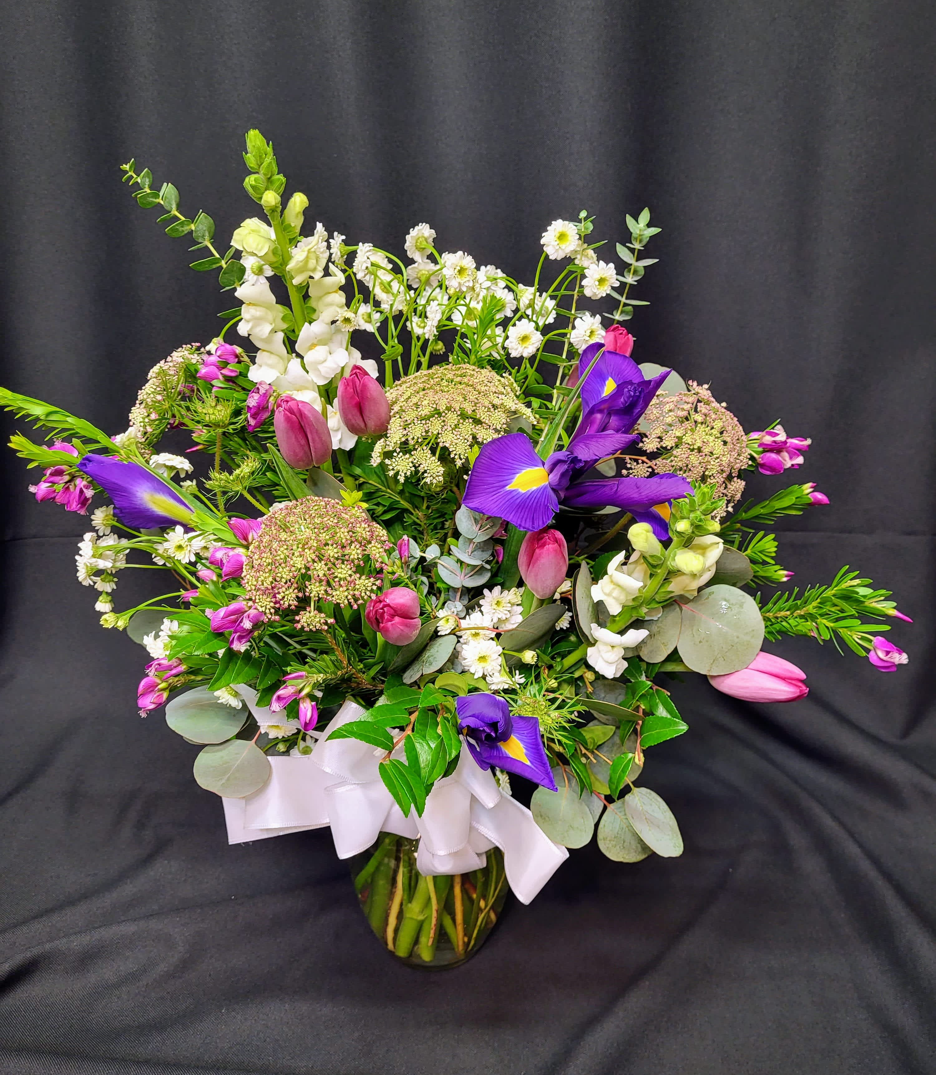 Mixed bouquet with purple irises, pink tulips, and white snapdragons in a glass vase