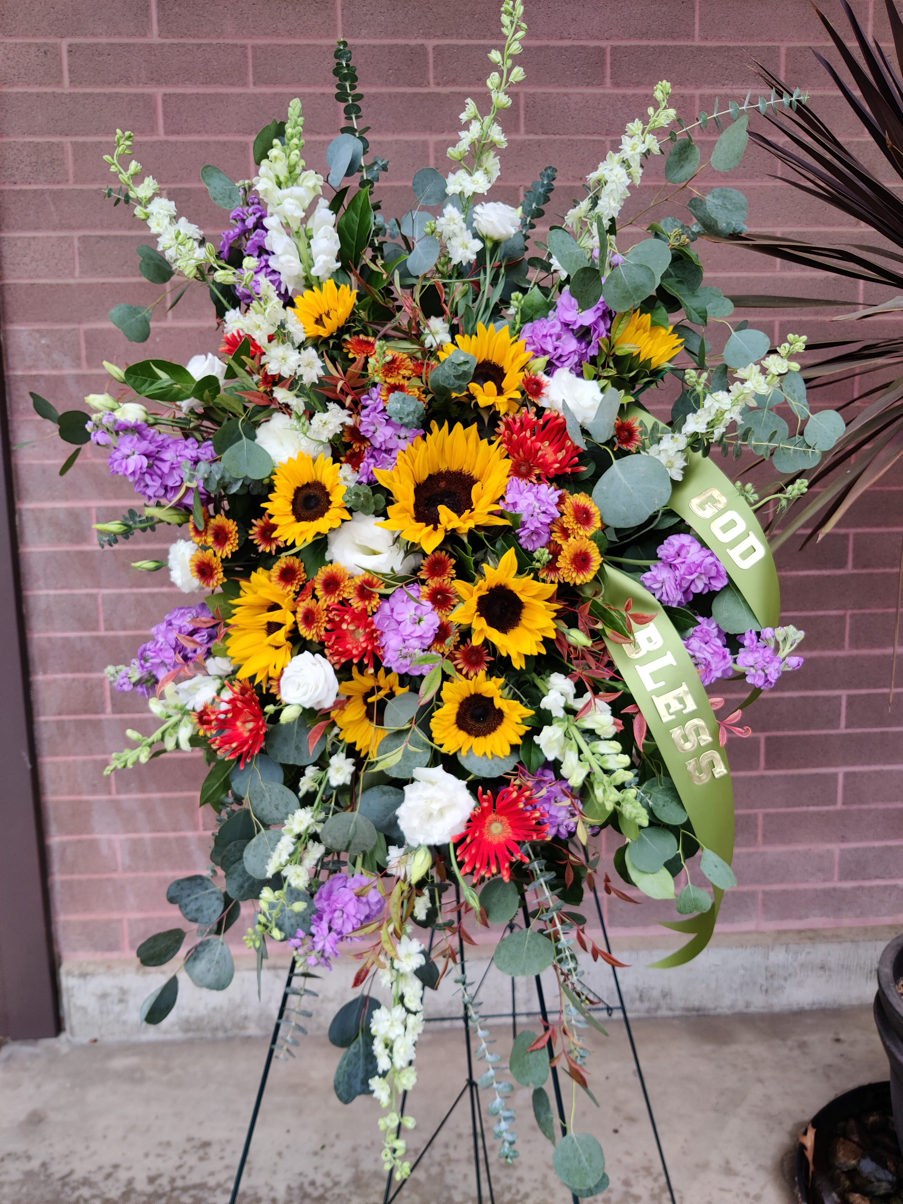 Large Seasonal Spray on Easel with Banner - One of our largest sympathy designs. Flowers and colors will vary based on the season. Seasonal flowers are an appropriate and elegant choice any time of year. Lovely combination of colors and textures for a most pleasing display 