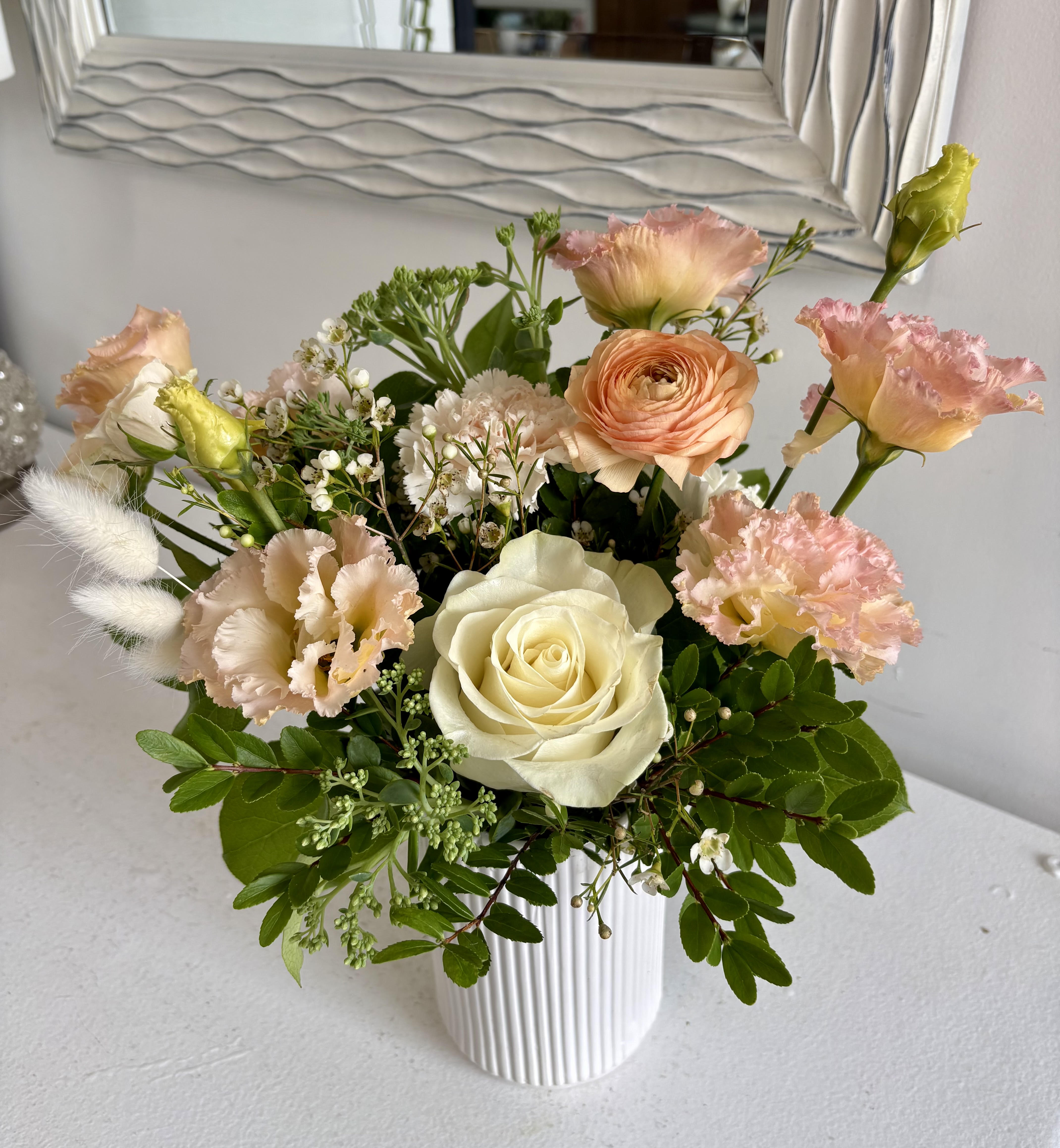 Mixed bouquet of cream roses and peach-pink blooms in a white ribbed vase