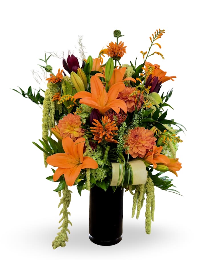 Orange lilies and mixed flowers arranged in a tall black vase