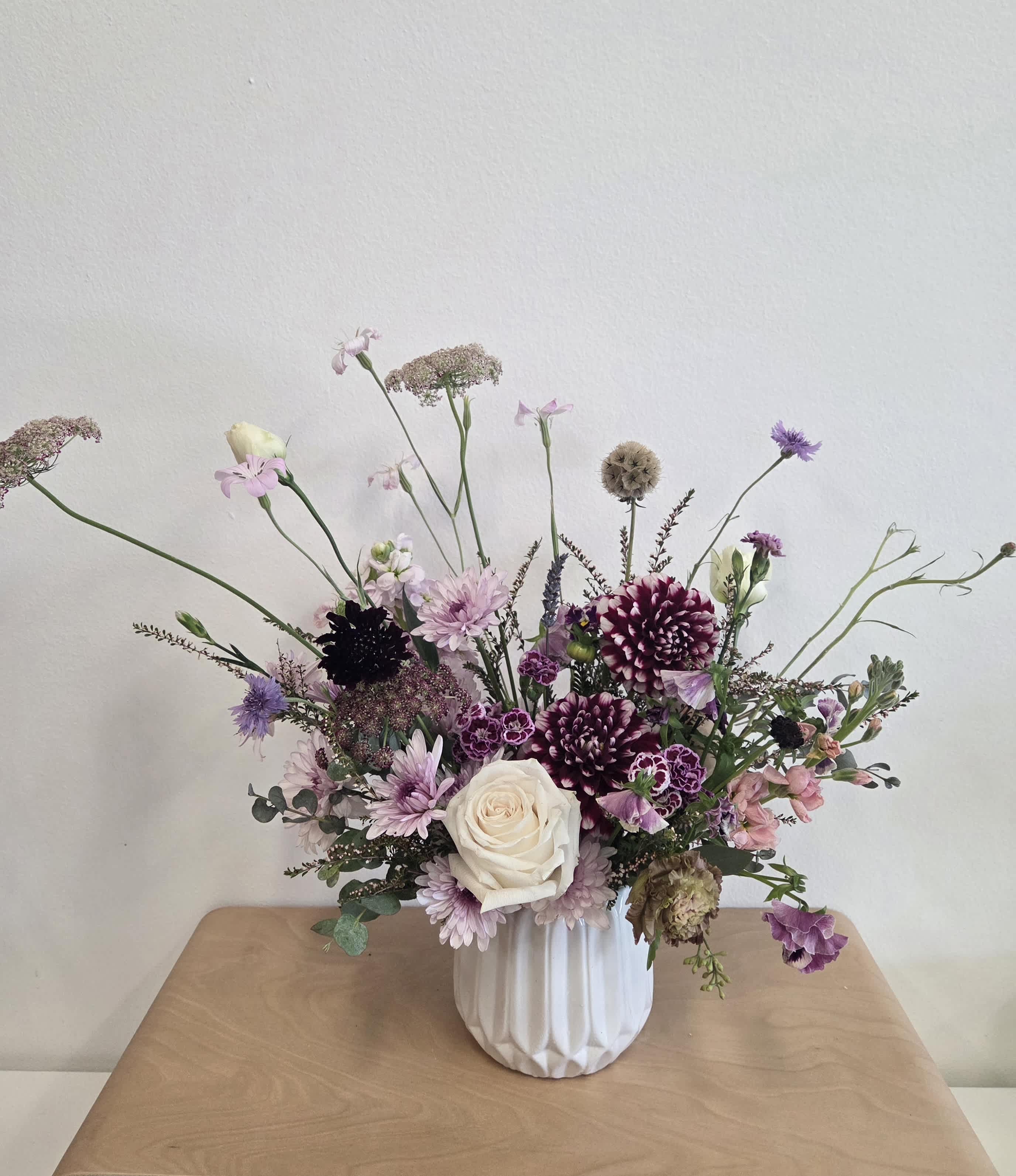 Mixed purple and white floral arrangement in a white vase