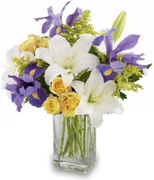 Mixed bouquet of white lilies, yellow roses, and purple irises in a clear glass vase