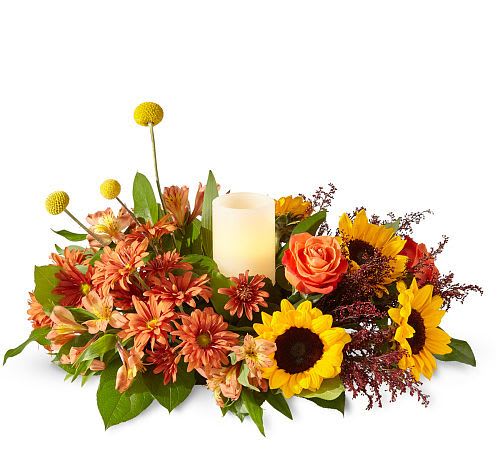 Honey Spark Centerpiece  - Ignite your unique fall flavour with the Honey Spark Centerpiece designed with a fresh take on fall classics like sunflowers and orange alstroemeria, arranged around an ivory pillar candle. 