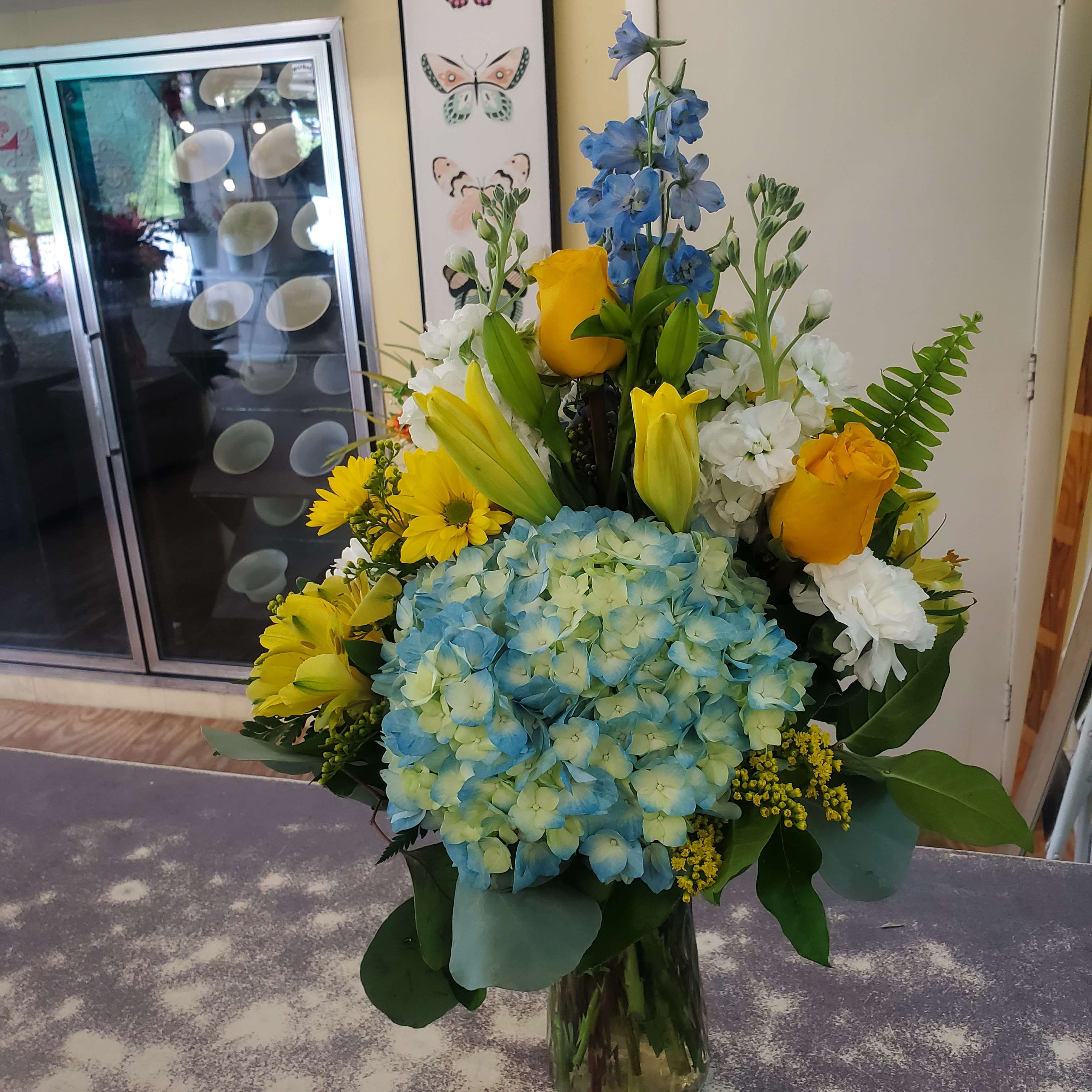 Blue hydrangeas with yellow roses and white flowers in a glass vase