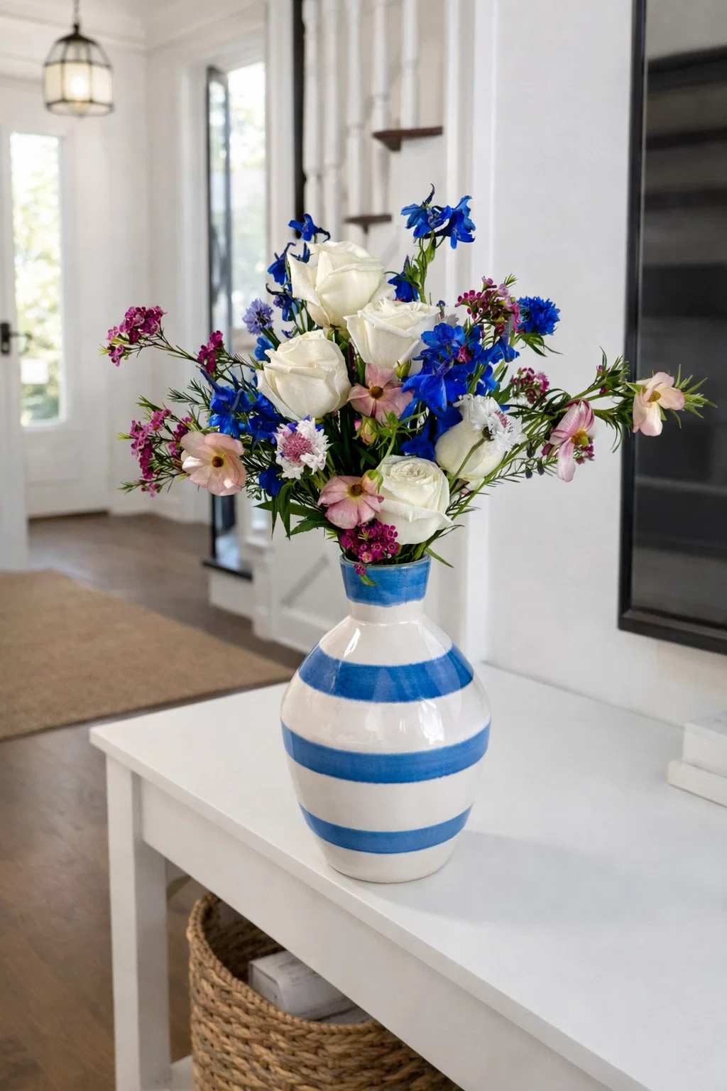 Bouquet of white roses, blue flowers, and pink blooms in a striped ceramic vase