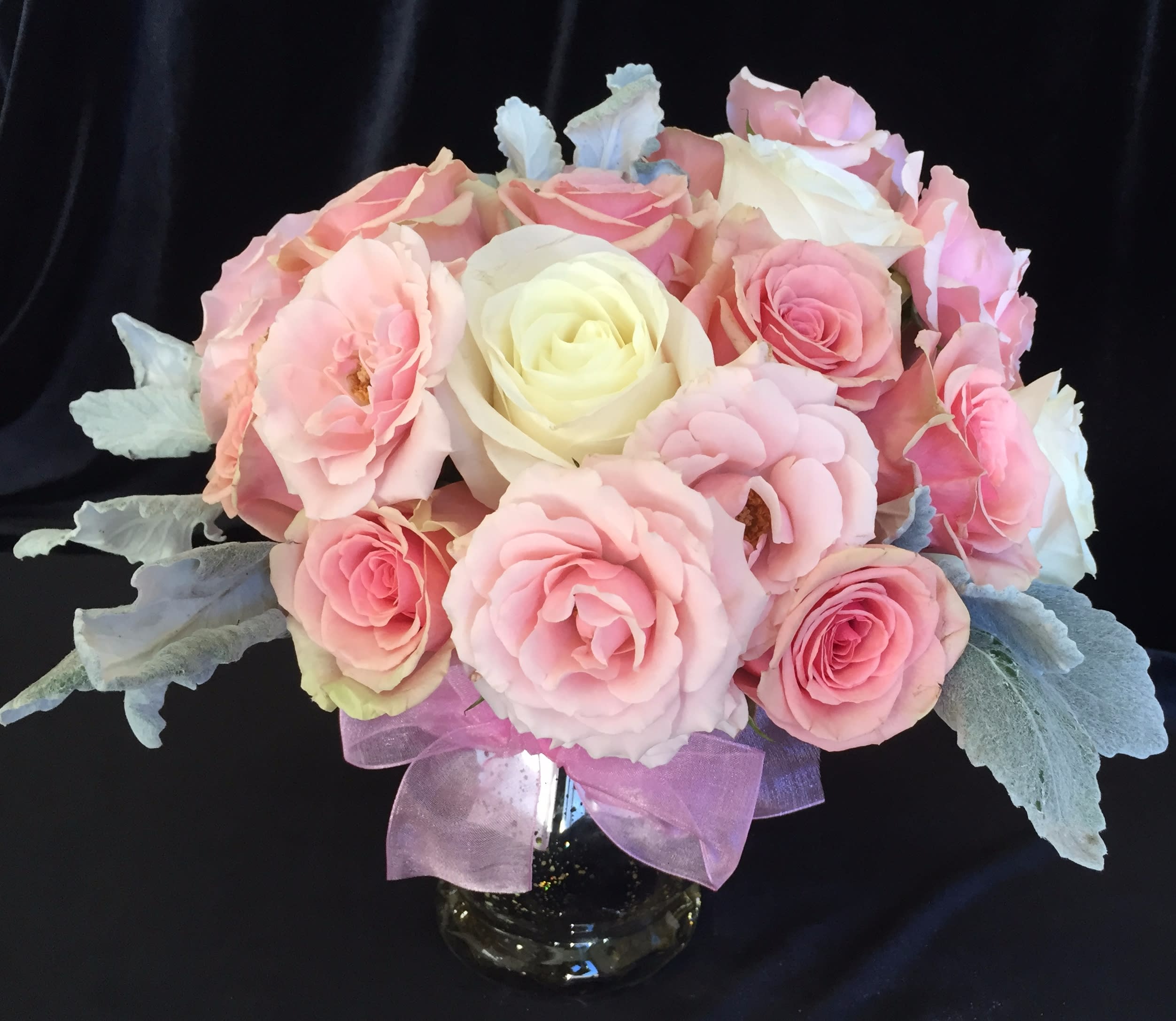 Pink and white rose bouquet in a glass vase with a purple ribbon