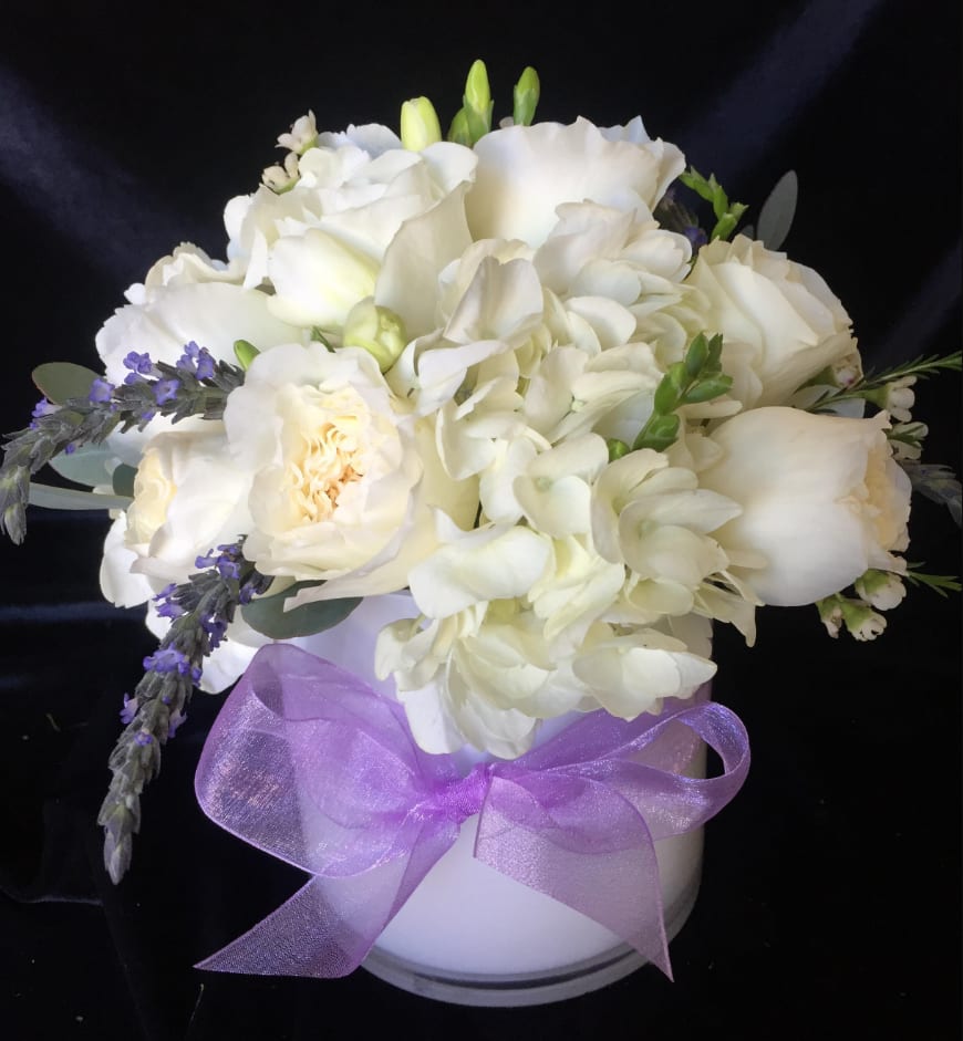 White floral bouquet in a white vase with a purple ribbon