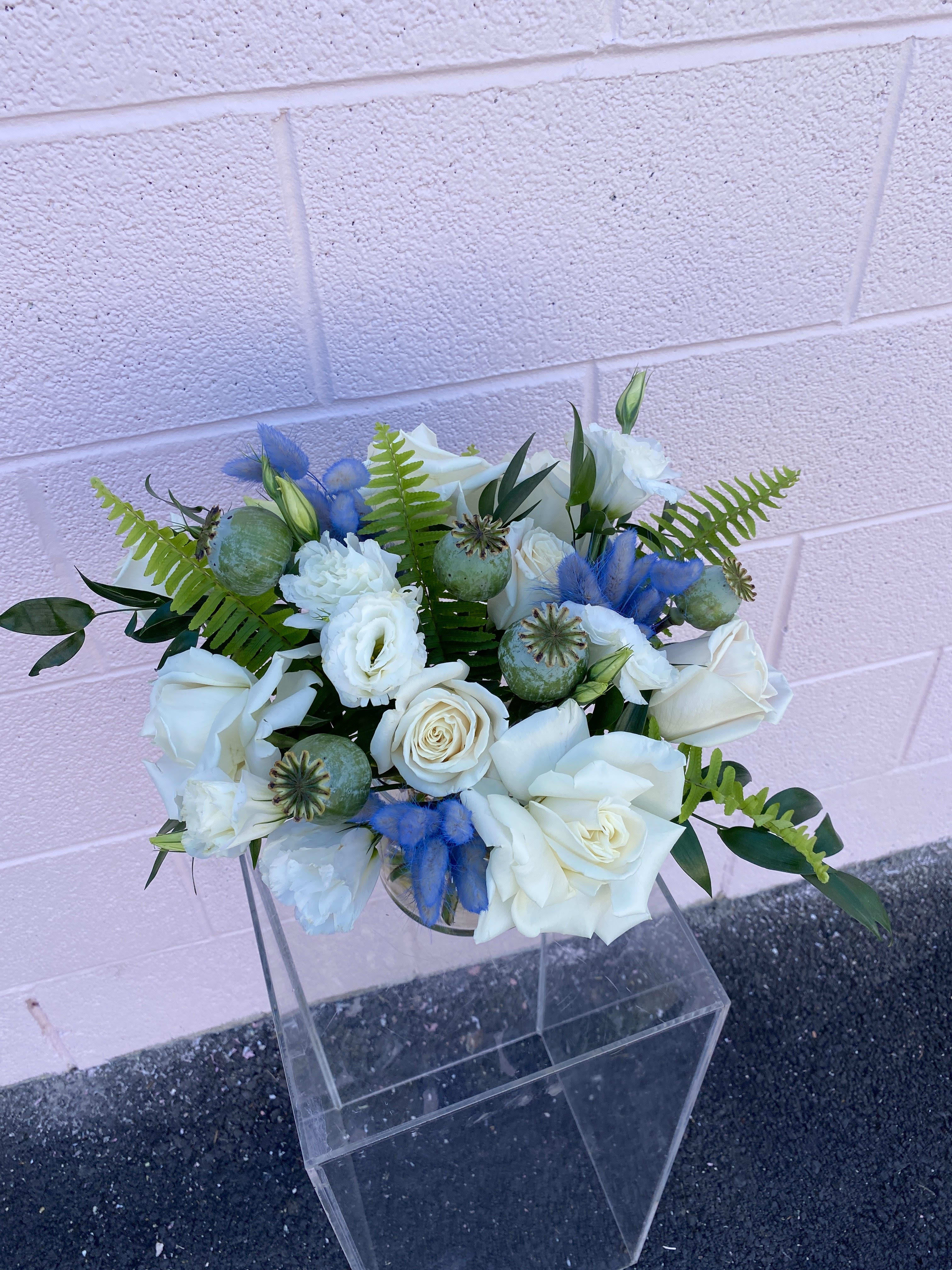 White rose bouquet with blue accents and green foliage in a clear vase