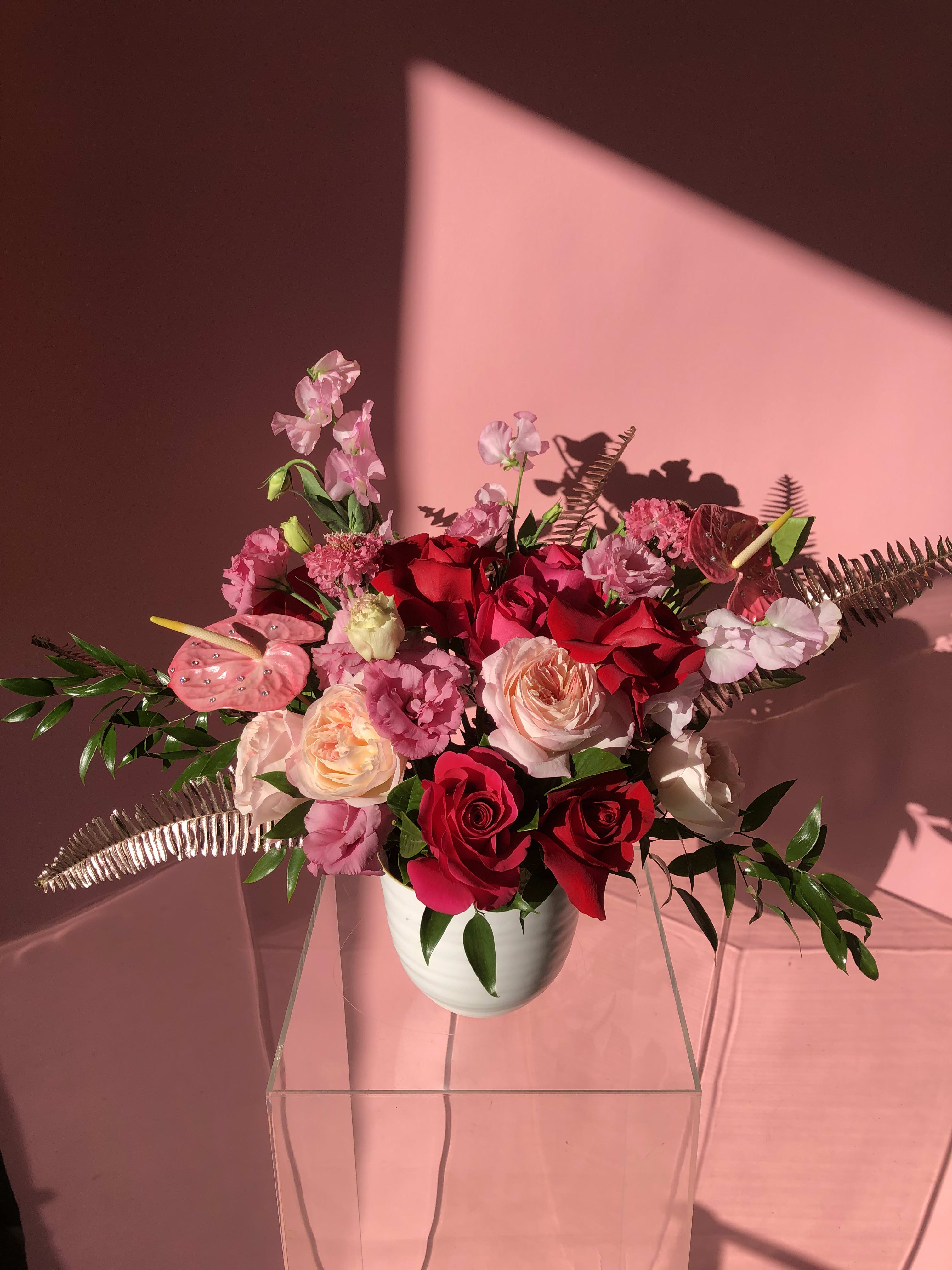 Pink and red rose arrangement in a white vase with tropical accents