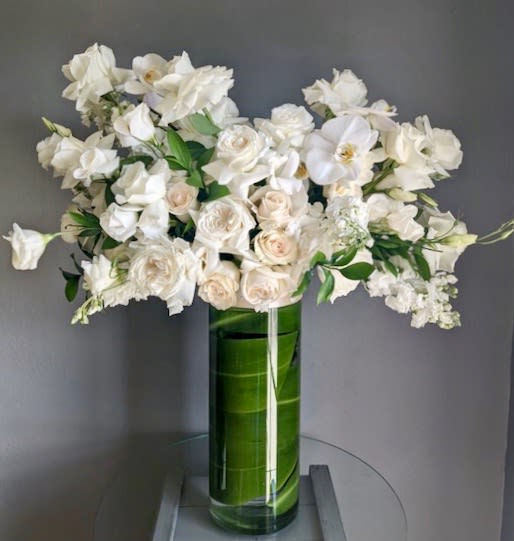 White roses and orchids arranged in a tall green glass vase