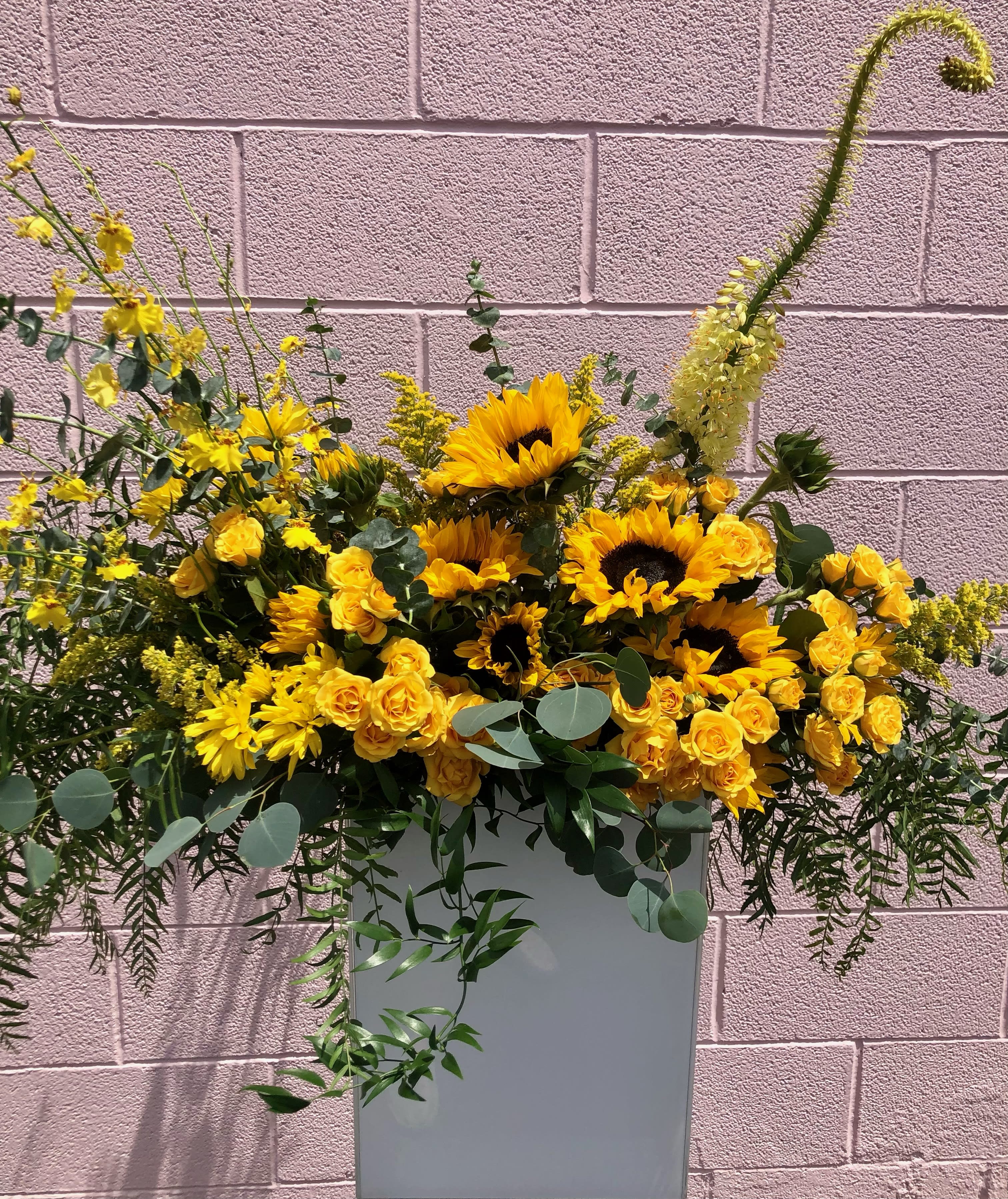 Yellow sunflowers and roses arranged in a tall white vase