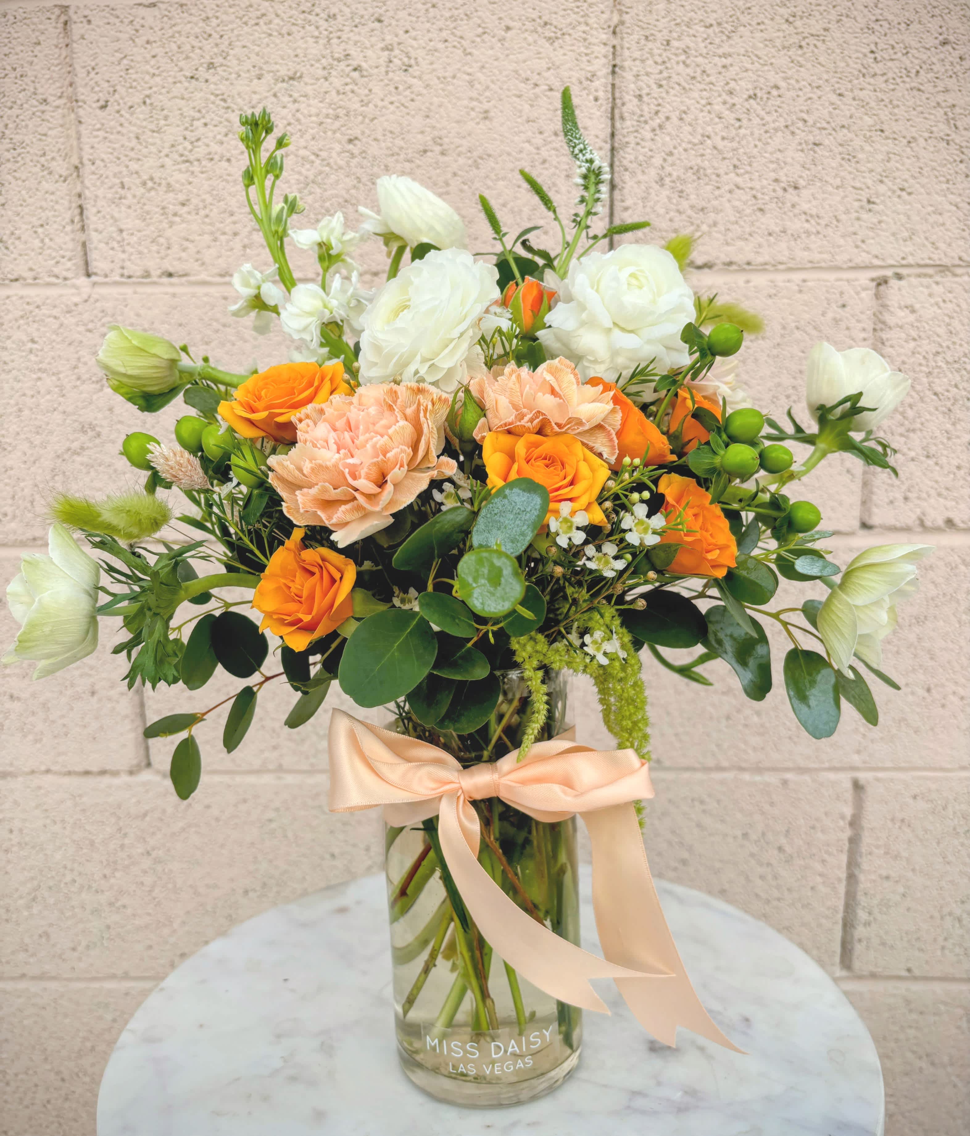 Orange and white flower bouquet in a glass vase with a peach ribbon