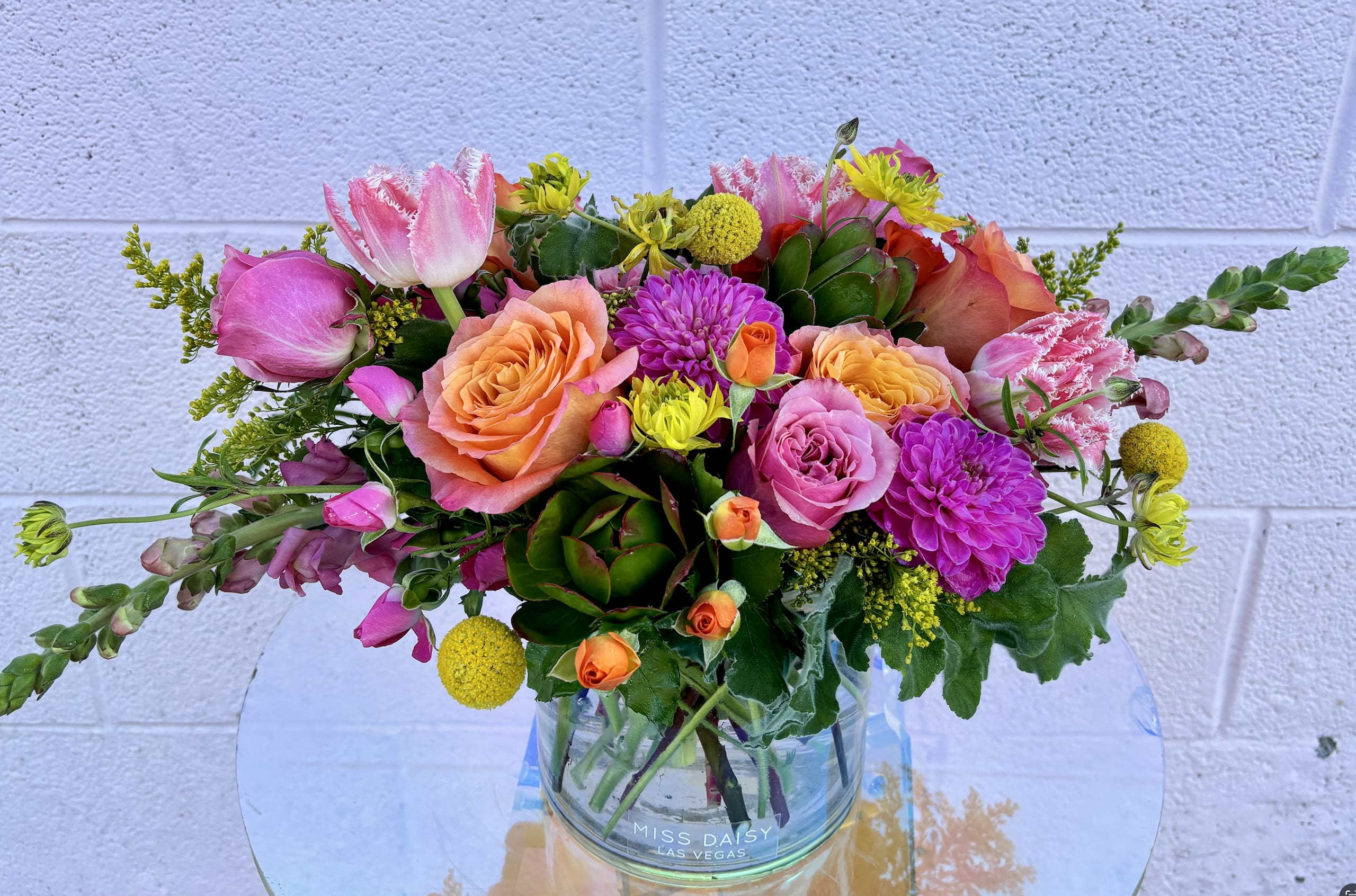Mixed bouquet of pink, peach, and yellow flowers in a clear glass vase