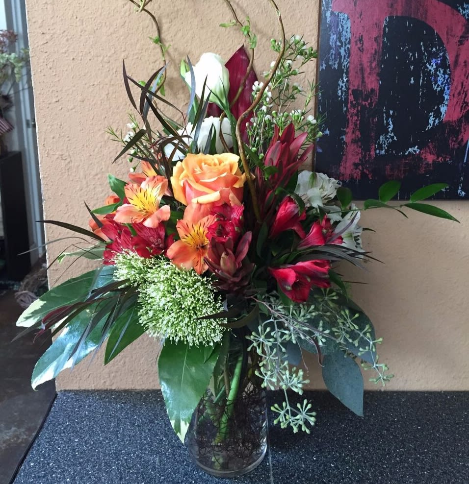 Tall mixed bouquet with orange roses and red lilies in a glass vase