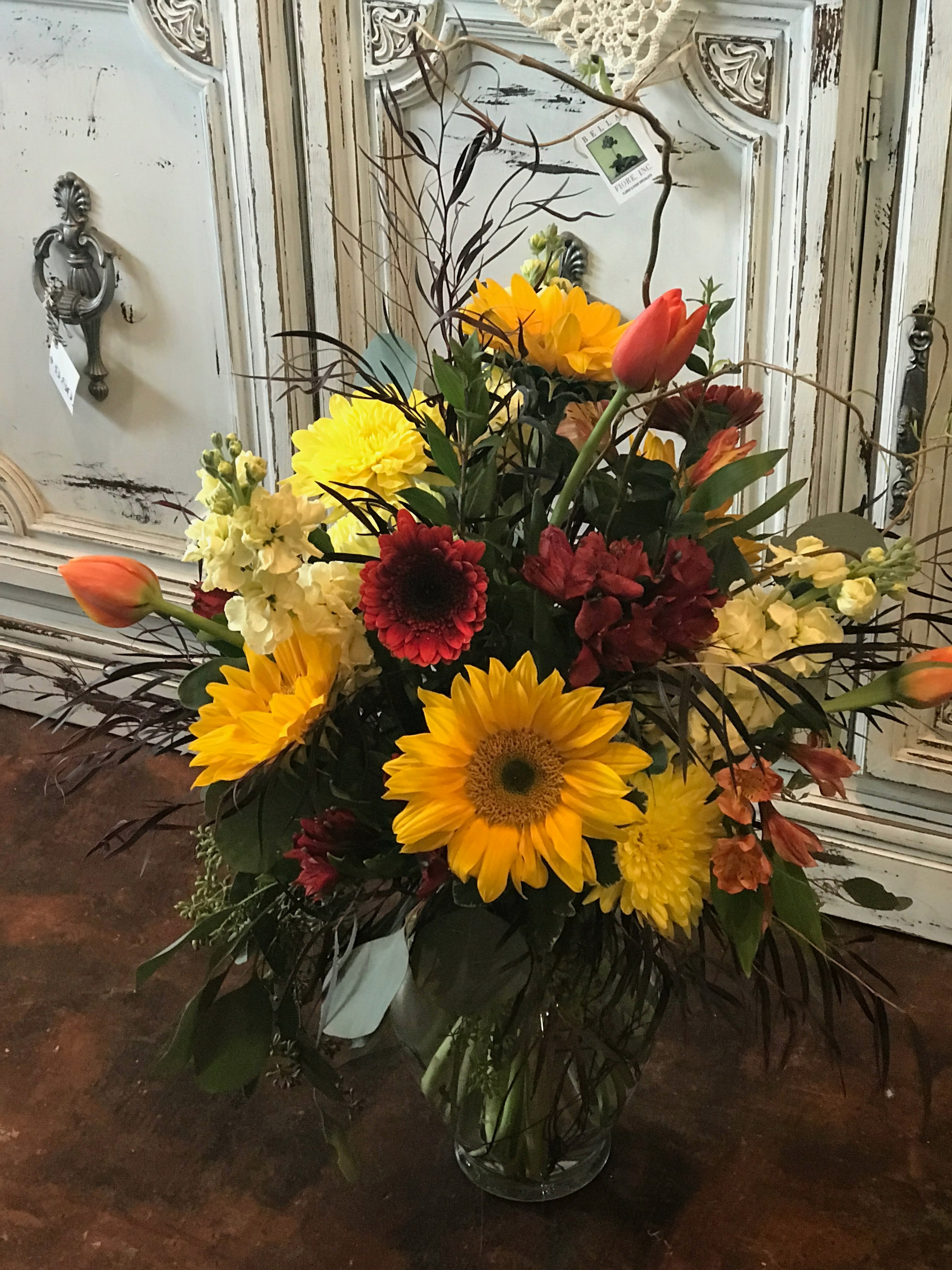 Bright mixed bouquet with sunflowers, tulips, and red blooms in a glass vase