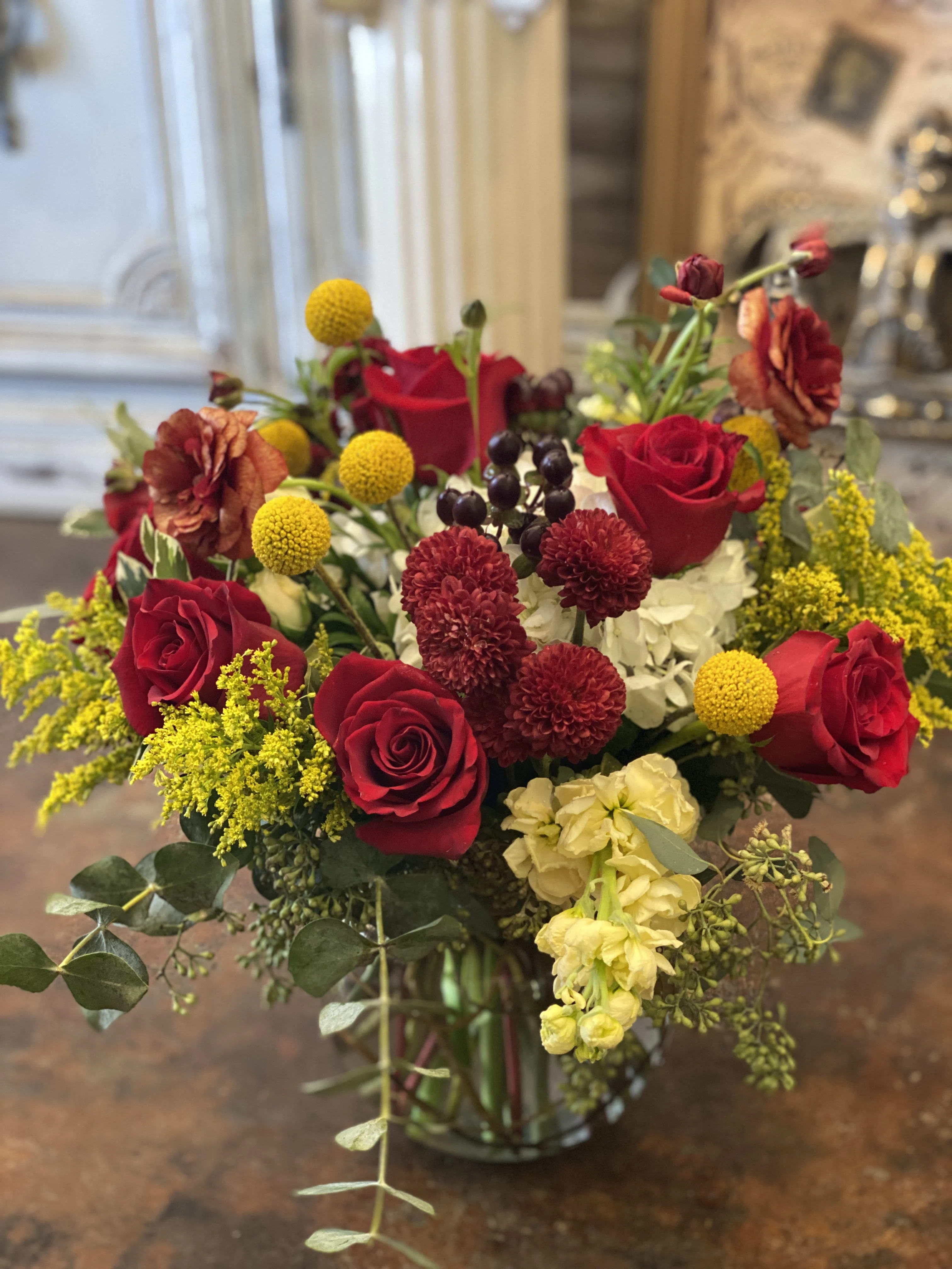 Bouquet of red roses, yellow billy balls, and mixed blooms in a glass vase