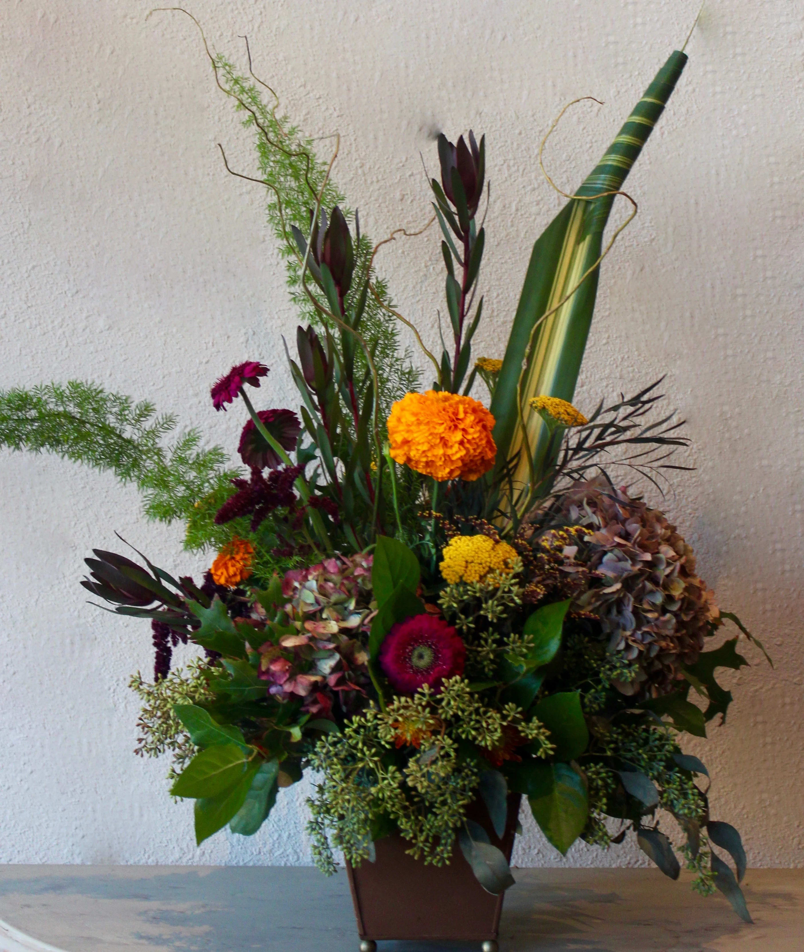 Tall mixed floral arrangement in a brown vase with orange and purple blooms