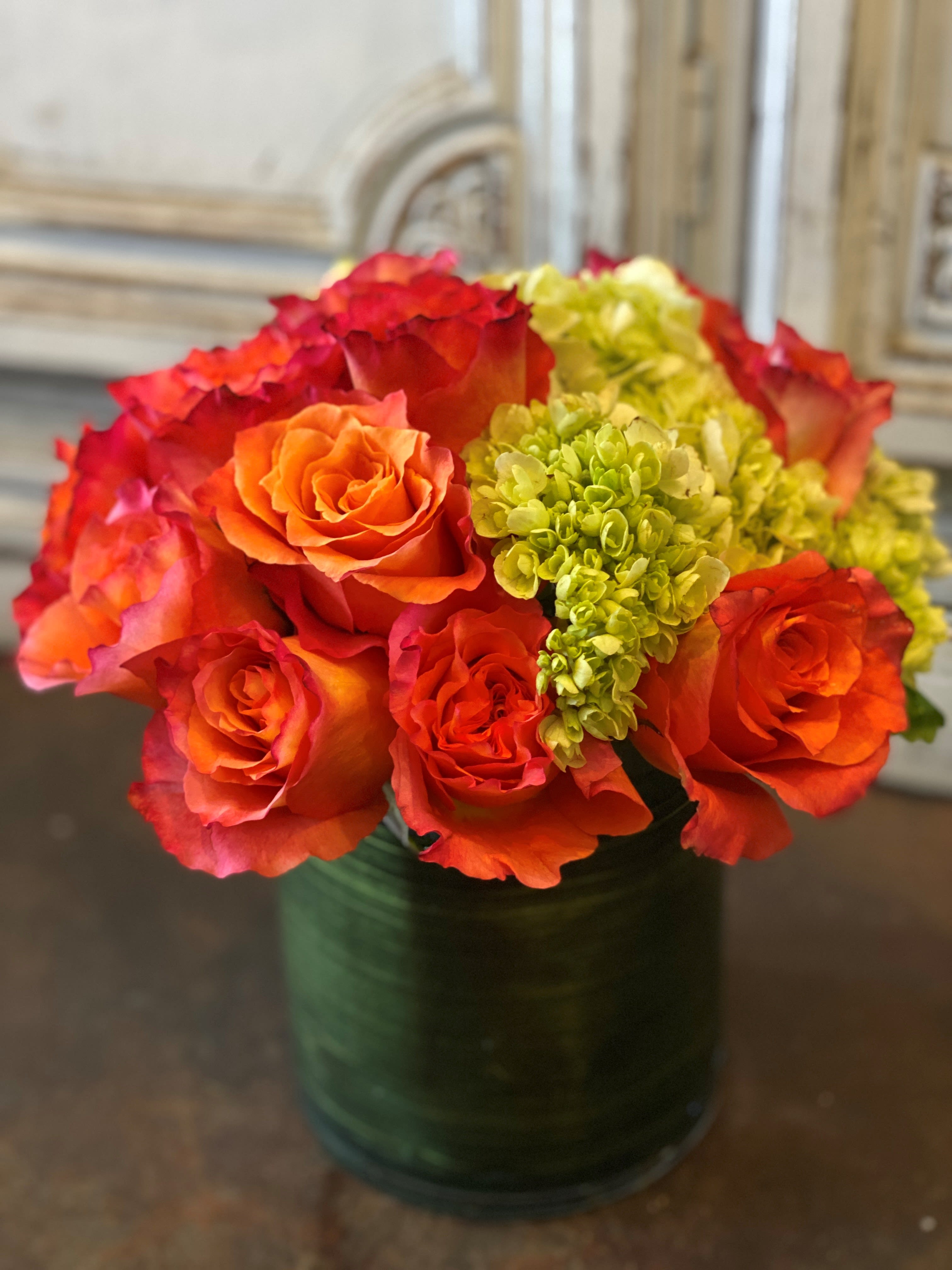 Orange and red roses with green hydrangeas in a glass vase