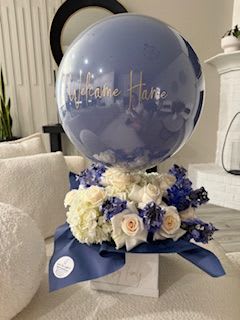 Blue balloon above white and blue roses in a gift arrangement