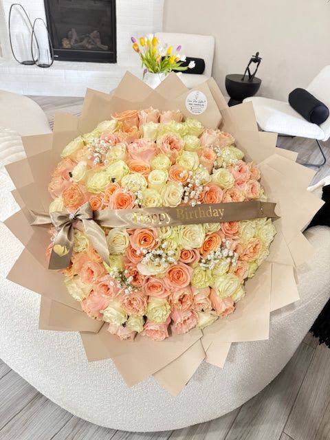 Large bouquet of peach and cream roses wrapped in tan paper with a birthday ribbon