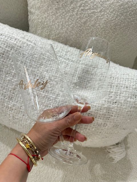 Two clear champagne flutes with gold script lettering held in a hand