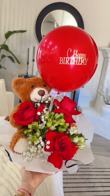 Teddy bear holding red roses with a birthday balloon