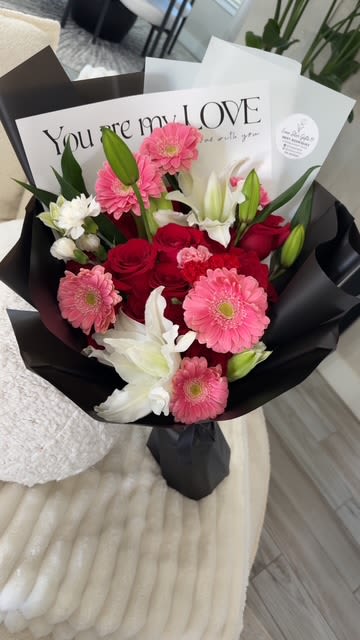 Bouquet of pink gerbera daisies, red roses, and white lilies in black wrap