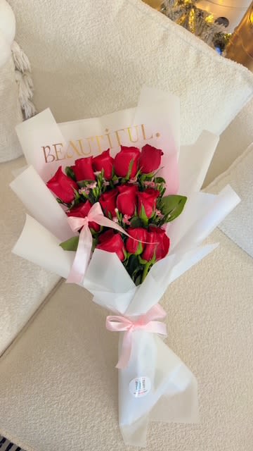 Bouquet of red roses wrapped in white paper with a pink ribbon