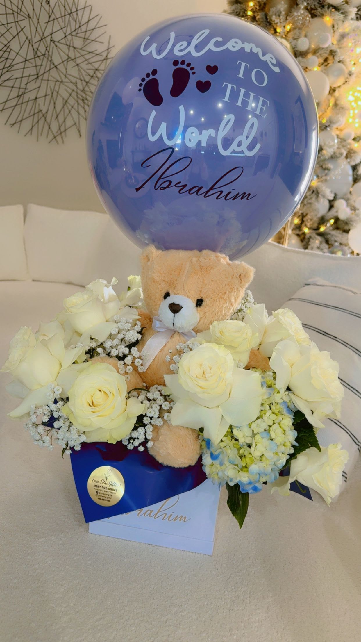 Teddy bear in white roses with a blue welcome balloon