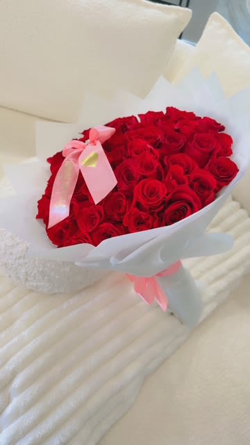 Bouquet of red roses wrapped in white paper with a pink ribbon