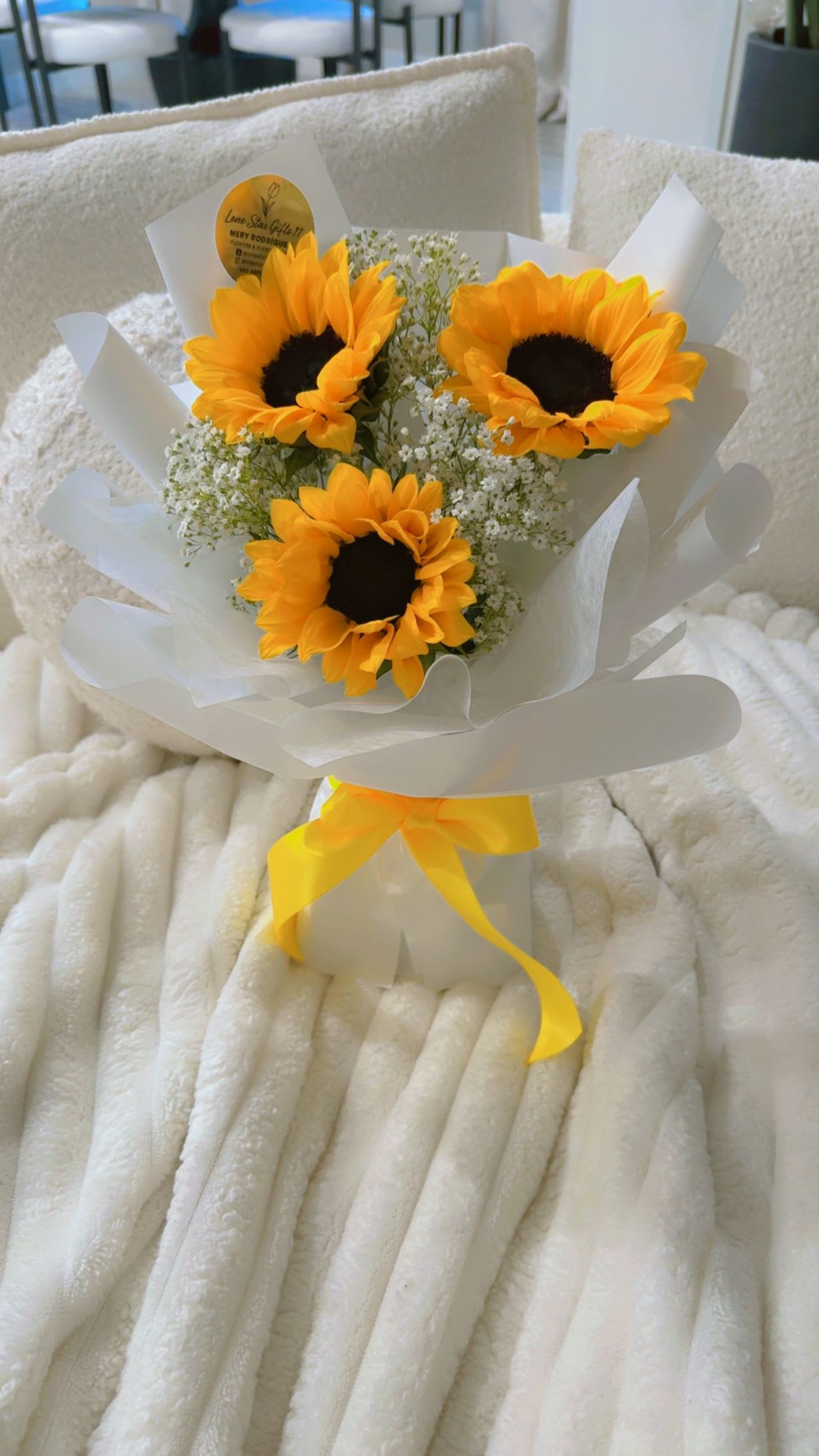 Bouquet of three sunflowers wrapped in white paper with a yellow ribbon