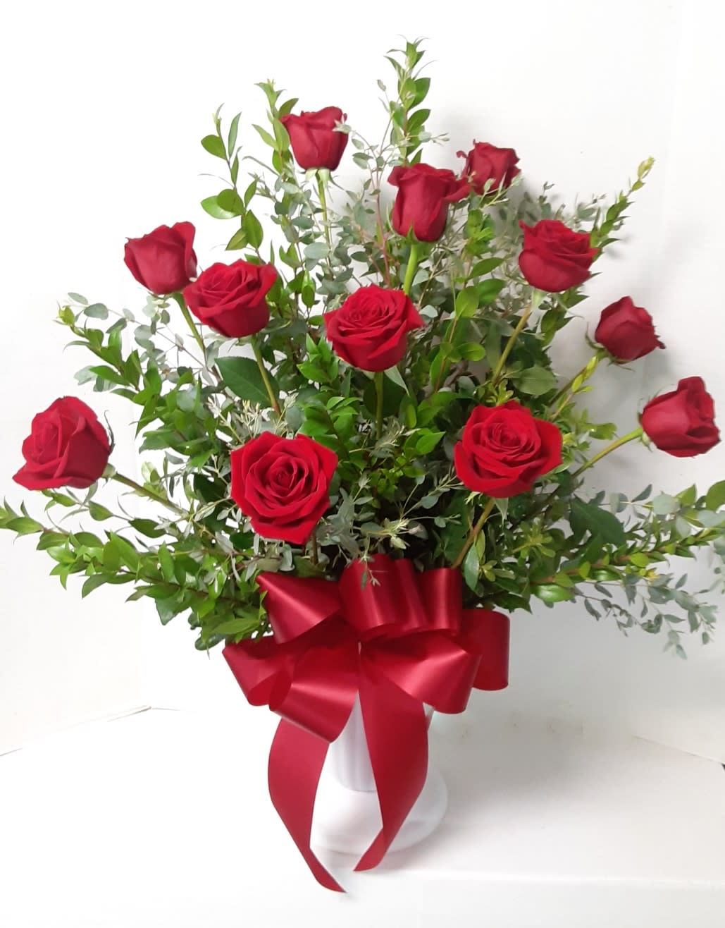 Red roses arranged in a white vase with a red ribbon bow