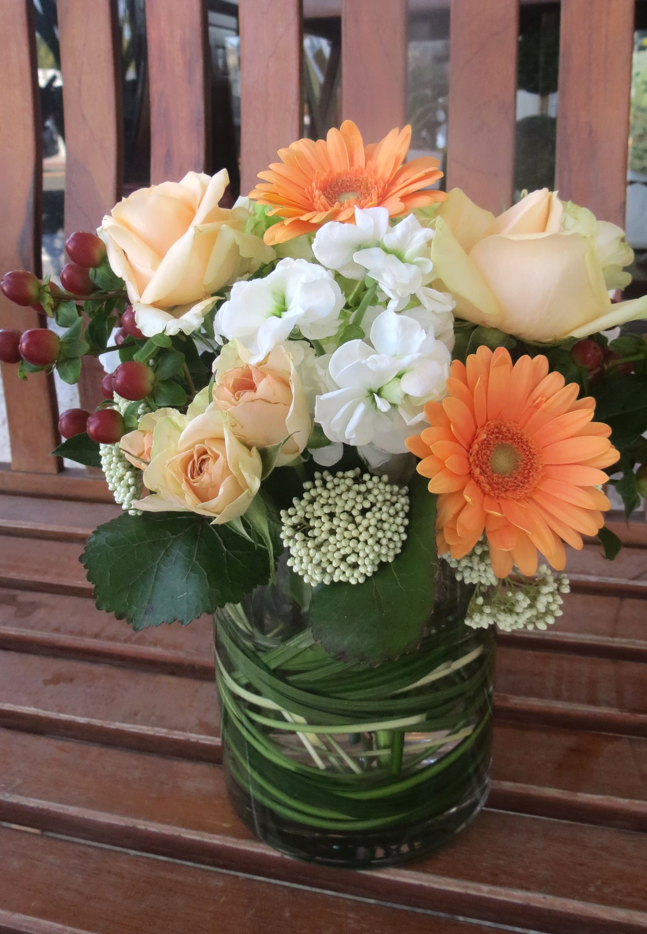 Bouquet of peach roses, orange gerbera daisies, and white flowers in a glass vase