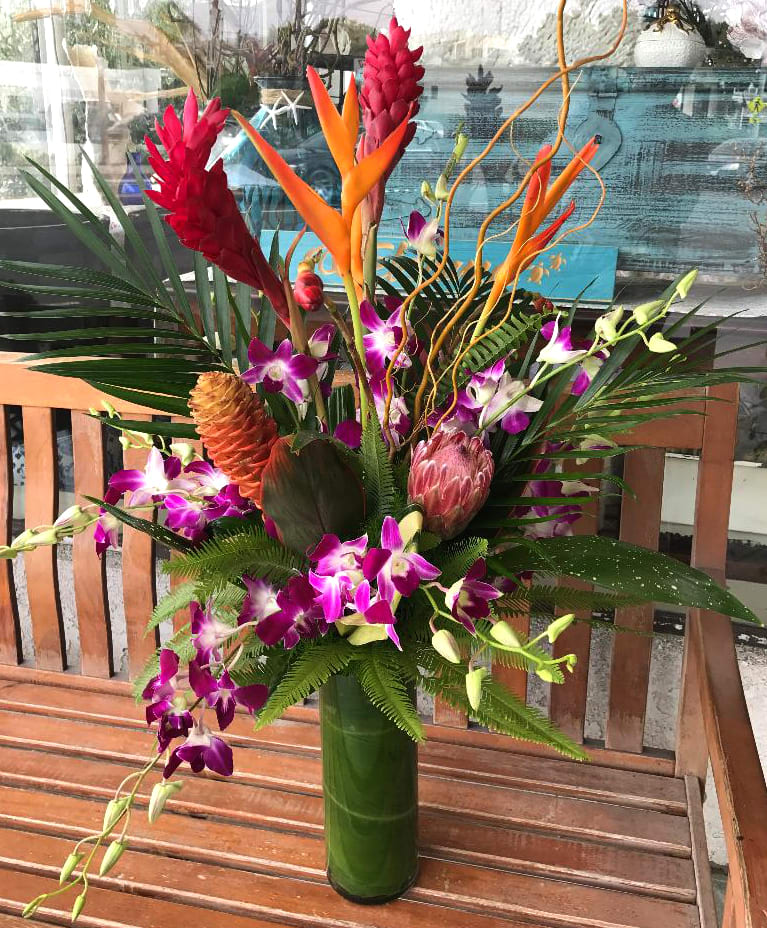 Tropical arrangement with purple orchids, red ginger, and orange heliconia in a tall vase