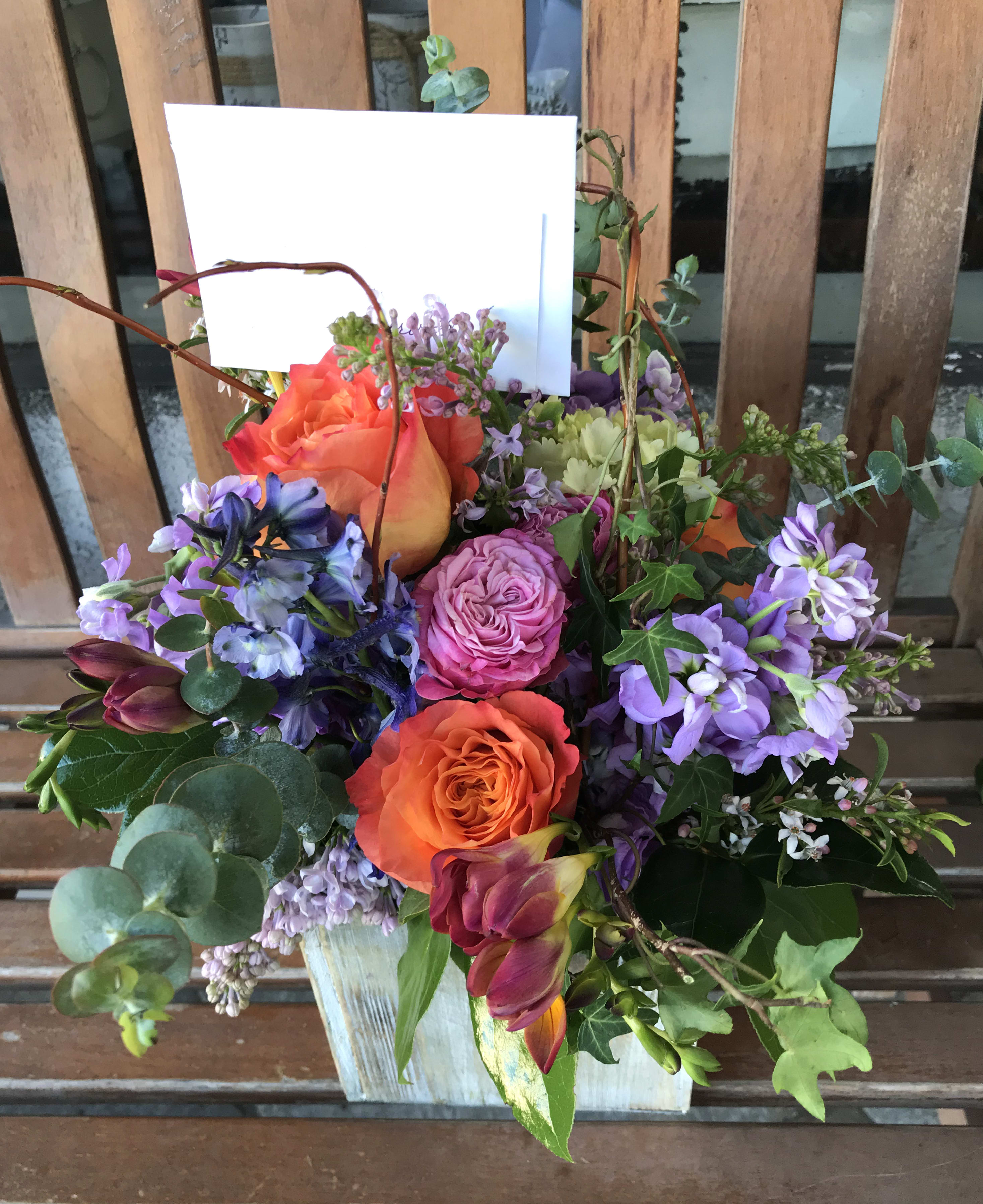 Mixed bouquet with orange and purple roses in a white container