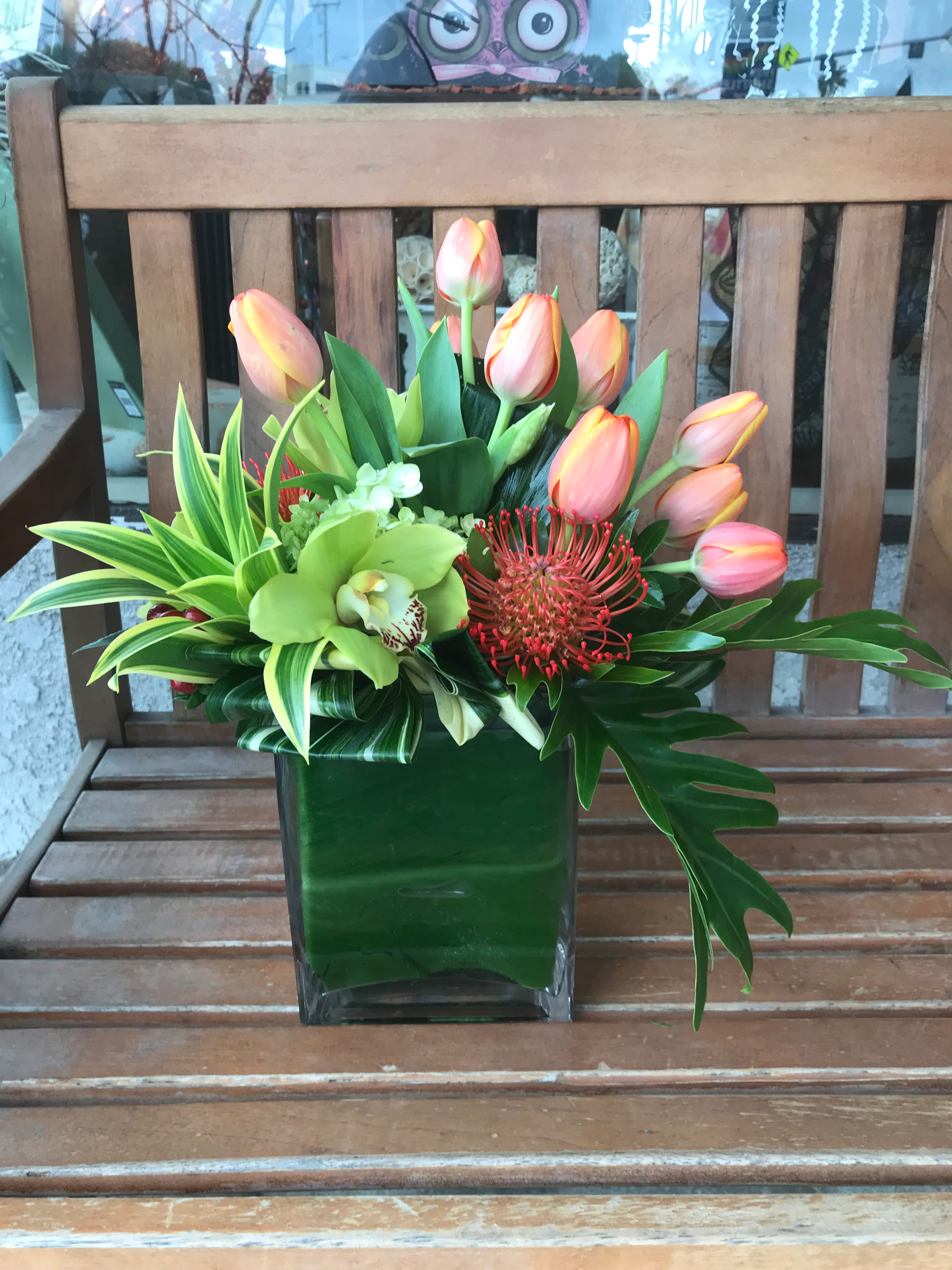 Pink tulips and tropical flowers arranged in a square glass vase