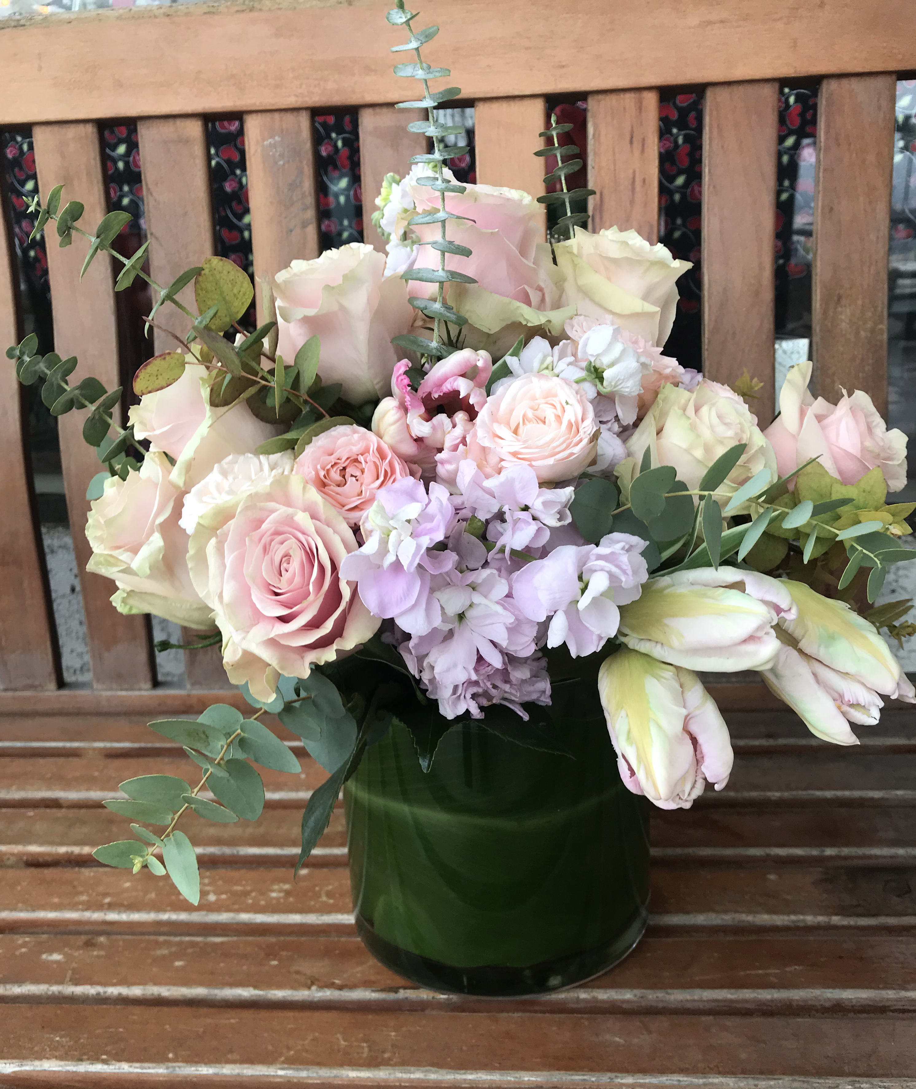Pink and cream roses with pale purple flowers in a green vase