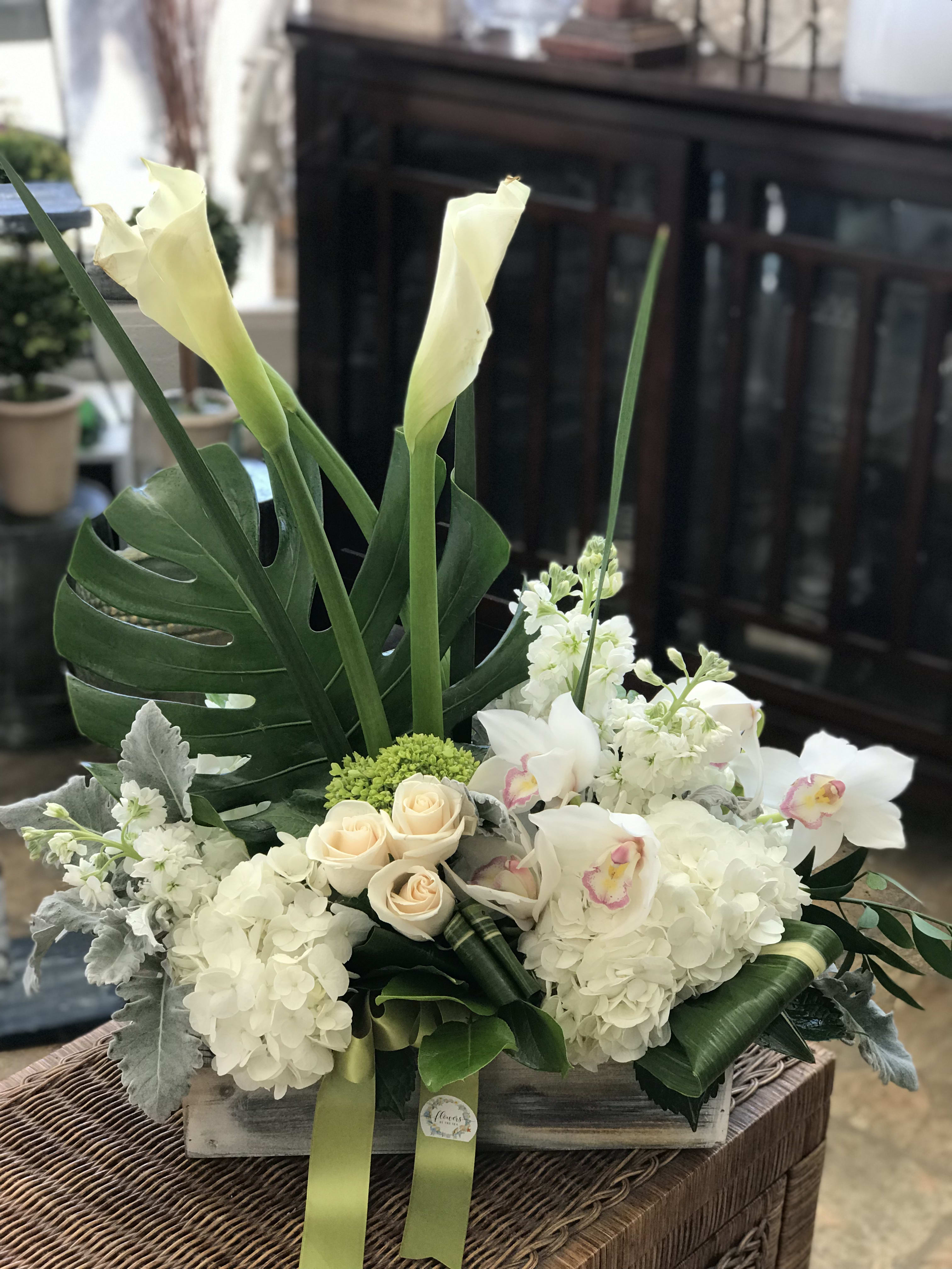 White floral arrangement with calla lilies, roses, and orchids in a wooden box