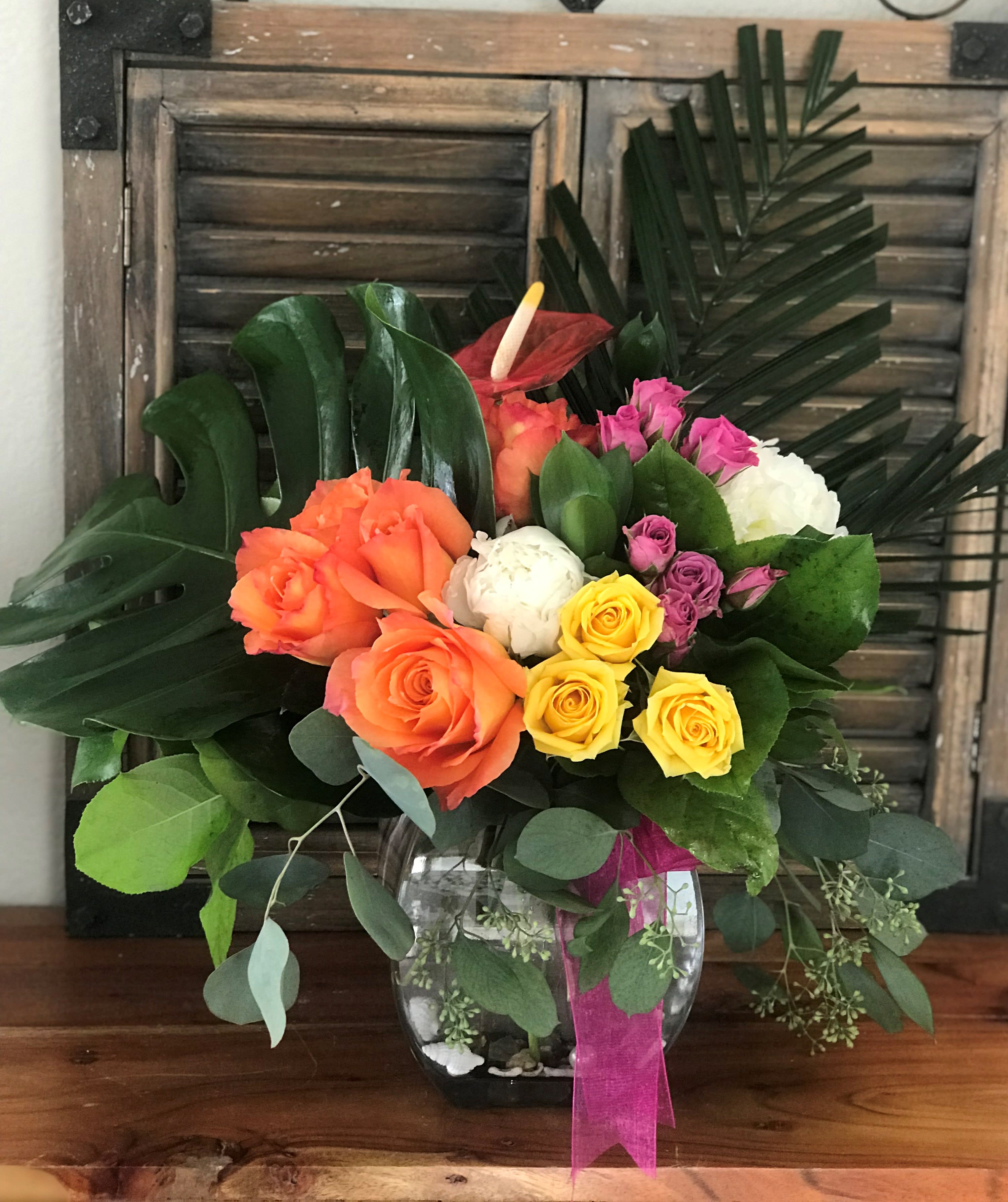 Colorful rose bouquet in a glass vase with tropical leaves