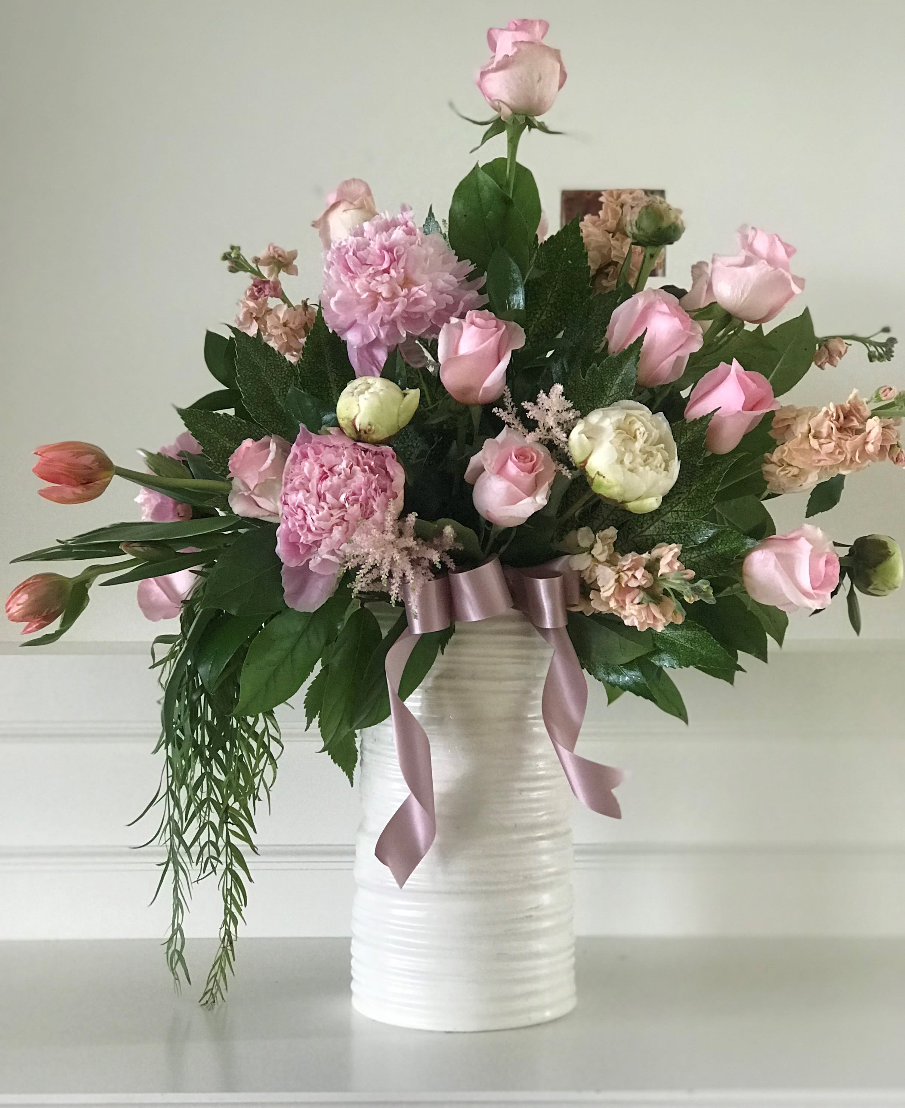 Pink roses and mixed blooms arranged in a white vase with a ribbon