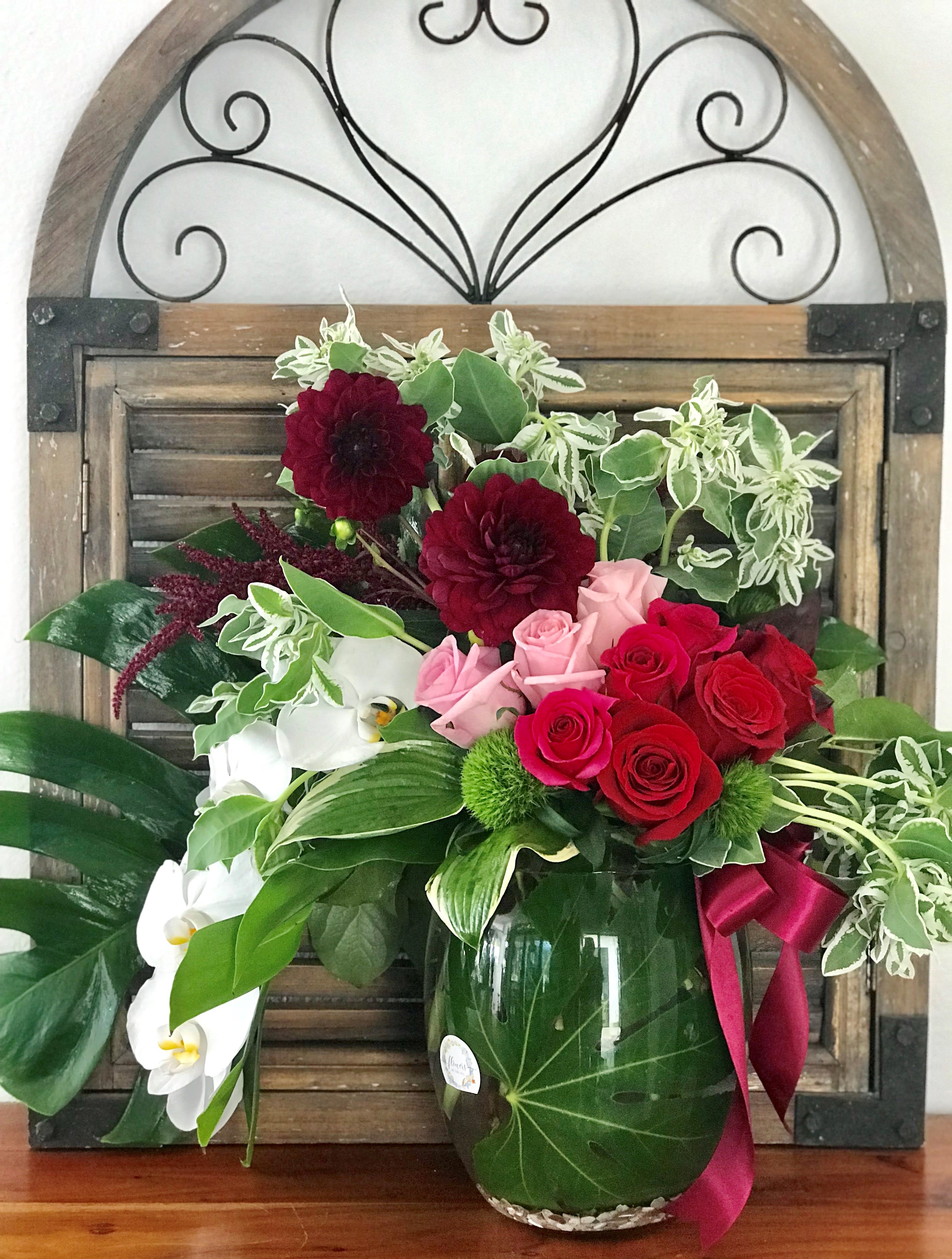 Bouquet of red and pink roses with white orchids in a glass vase