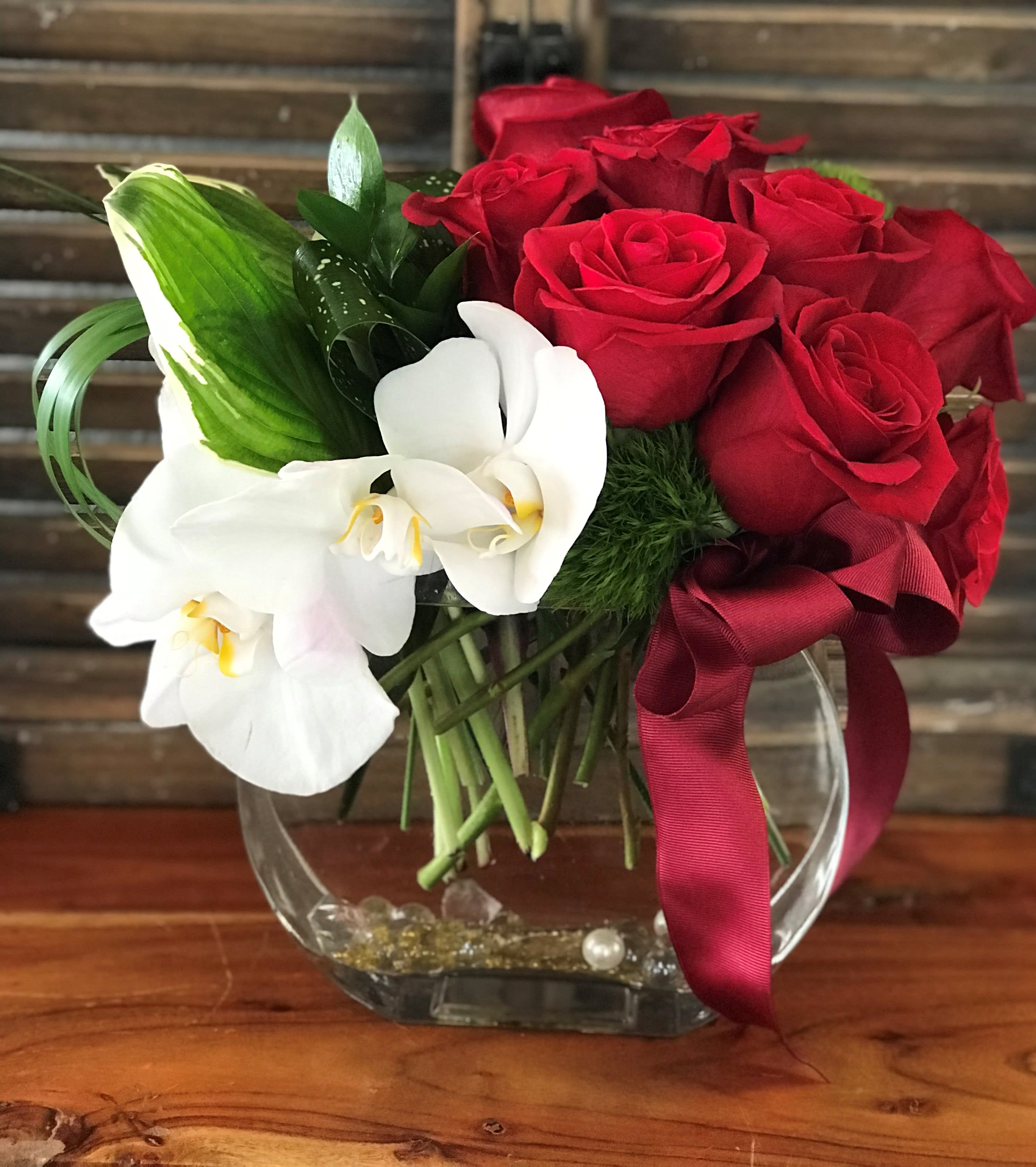 Red roses and white orchids in a clear glass vase with a burgundy ribbon