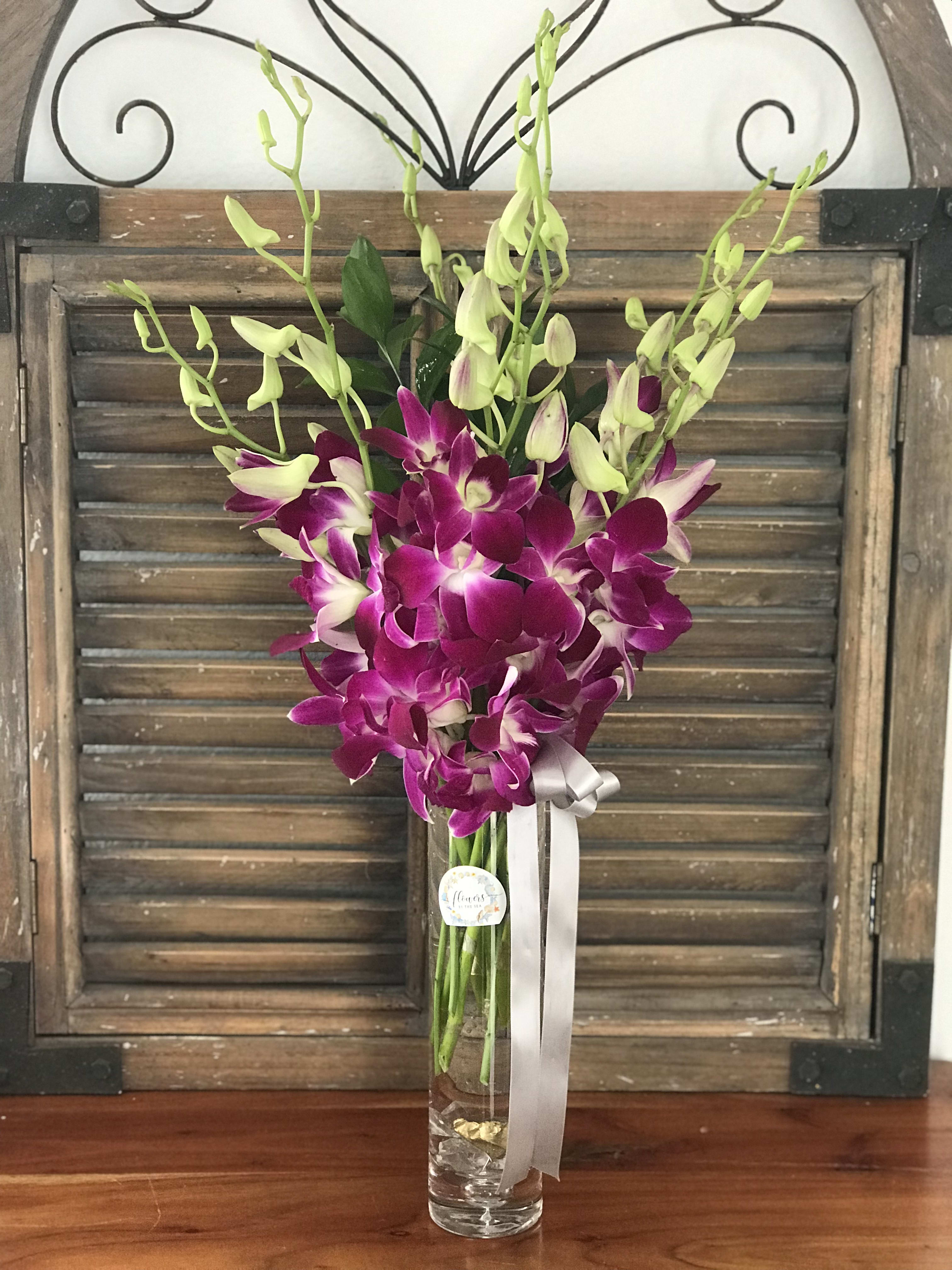 Purple and white orchids in a tall glass vase with a ribbon
