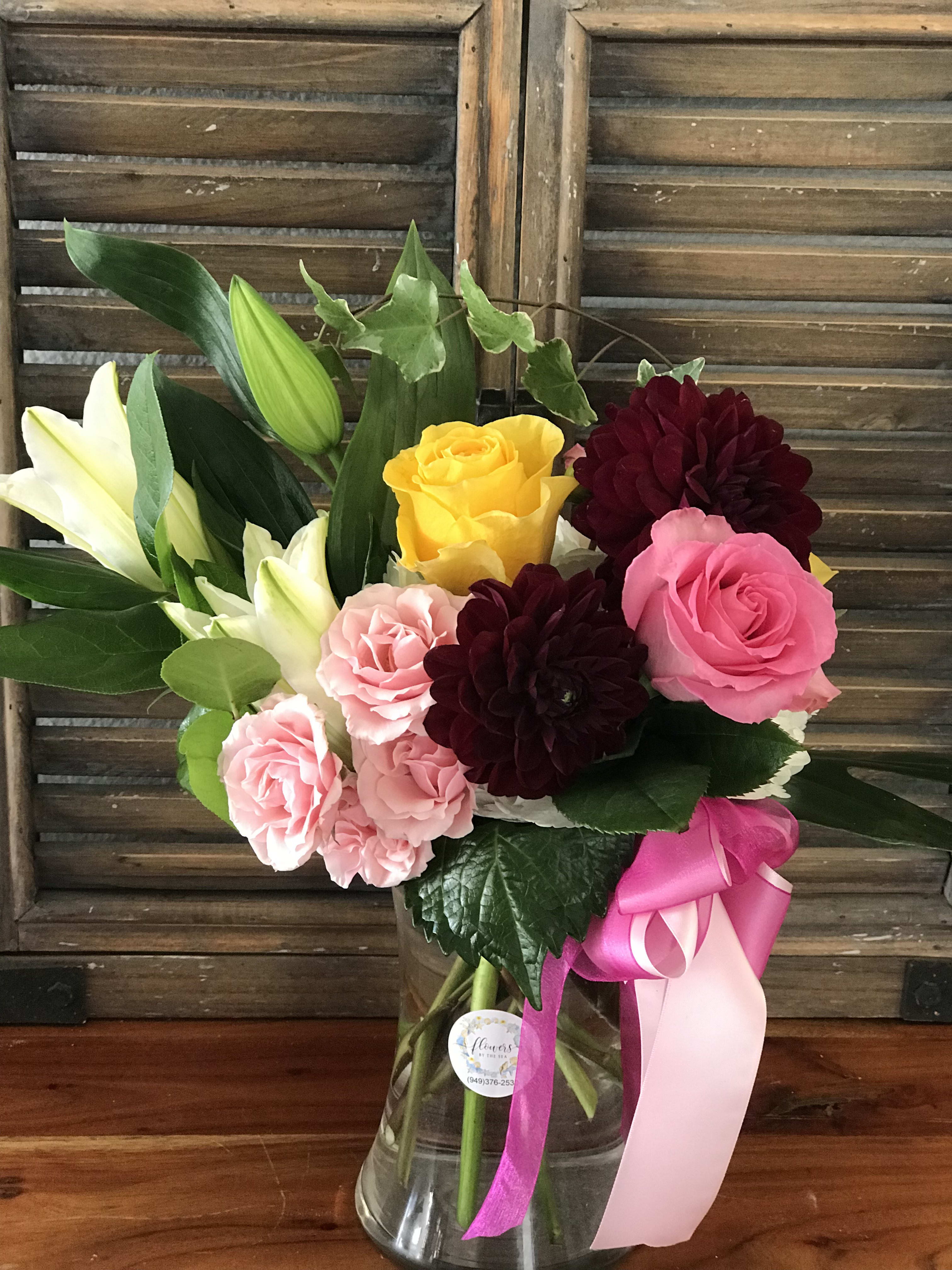 Bouquet of pink and yellow roses with white lilies in a glass vase
