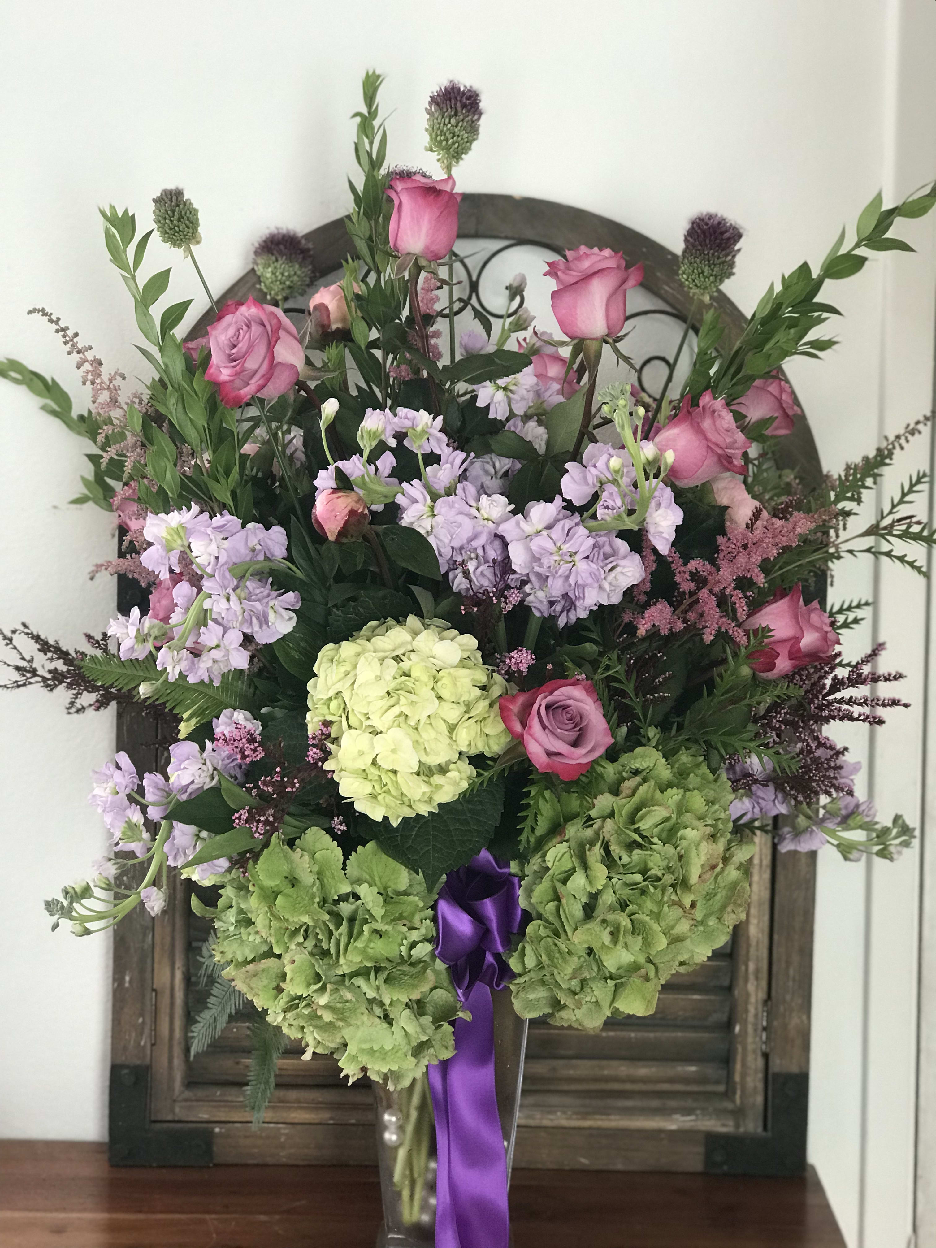 Pink roses and lavender flowers in a tall vase with green hydrangeas