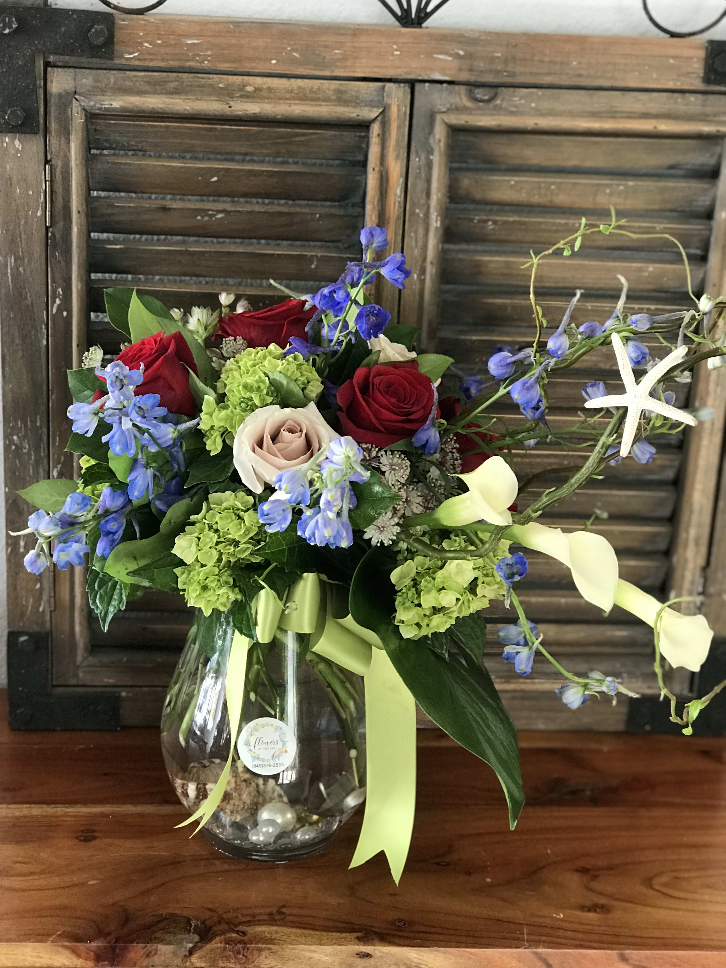 Bouquet of red and blush roses with blue flowers in a glass vase