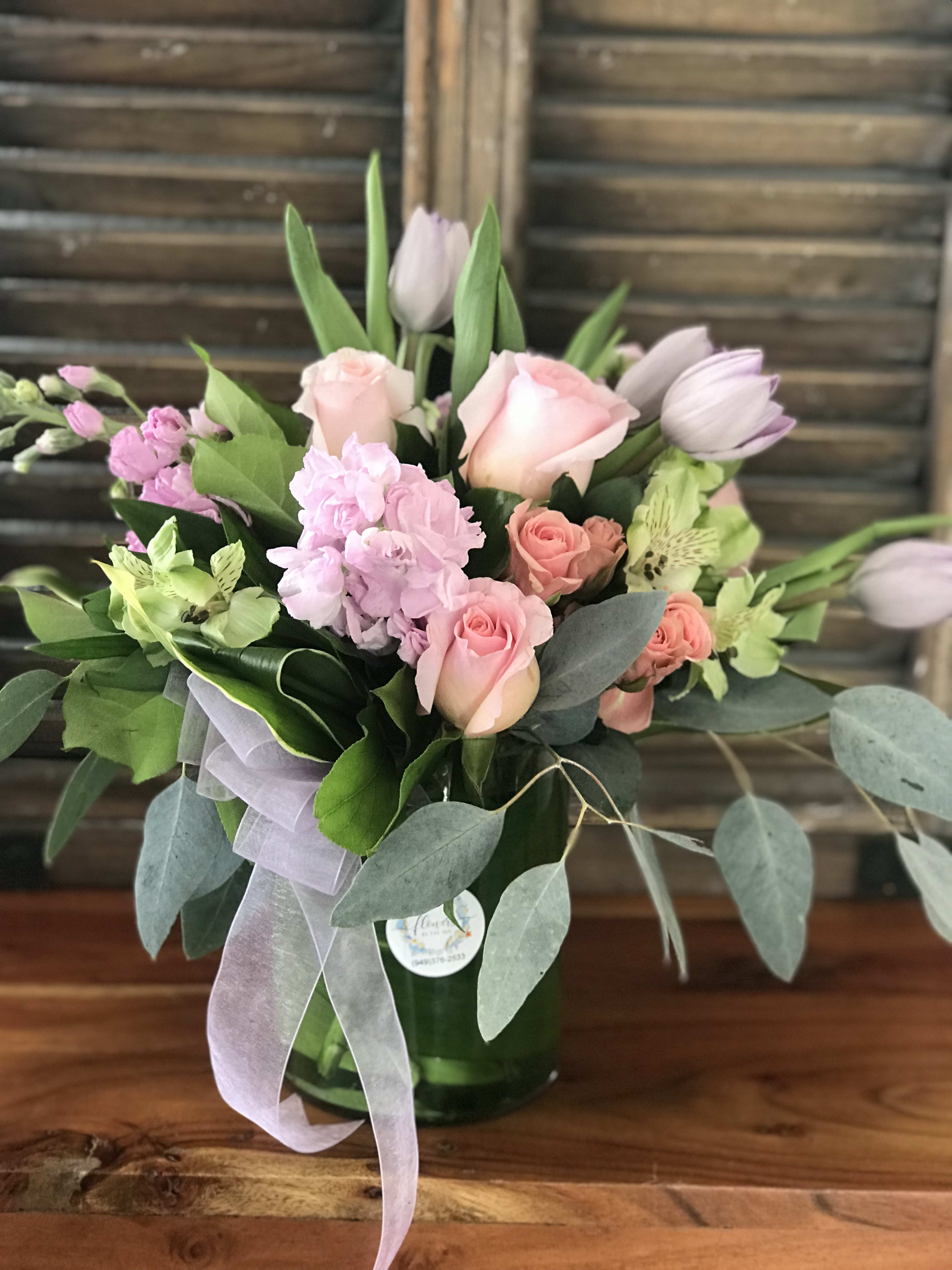 Pink roses and tulips arranged in a glass vase with ribbon