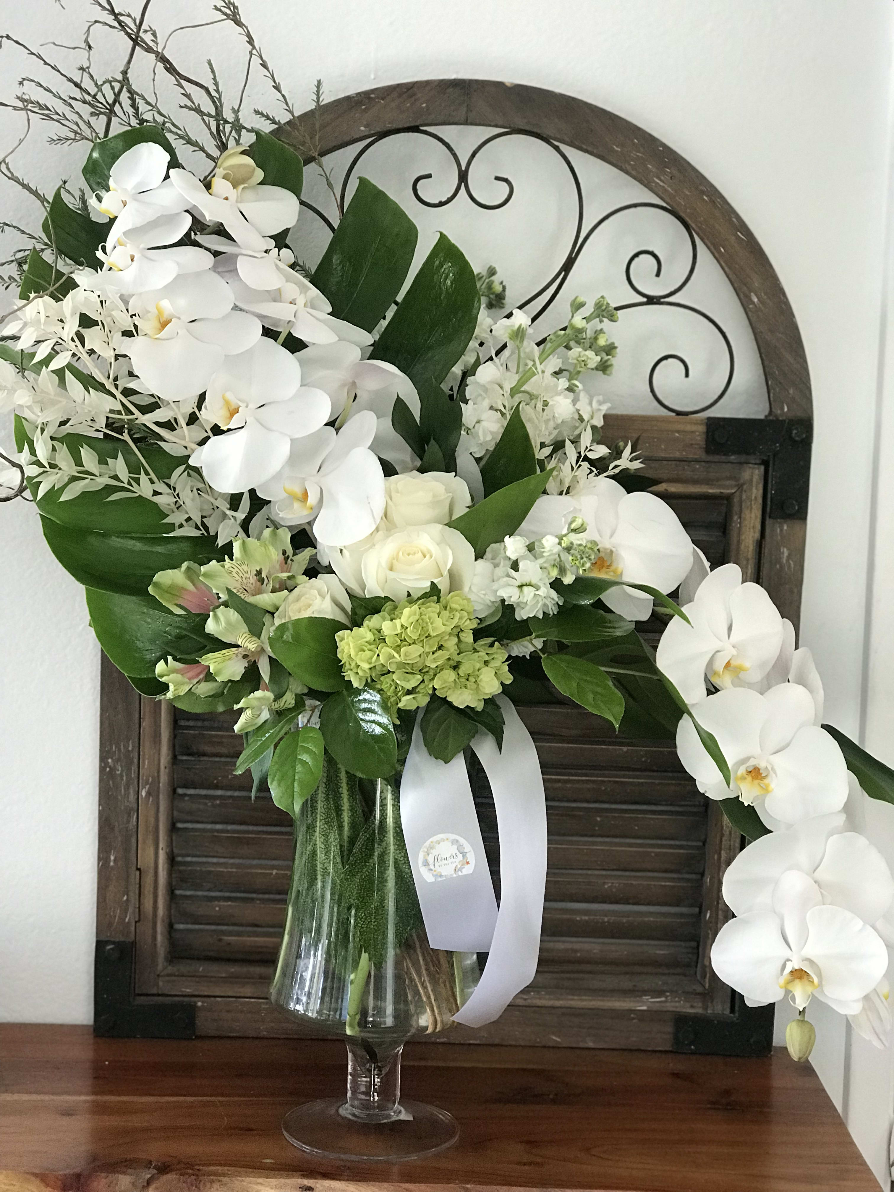White orchid and rose arrangement in a glass vase with green accents